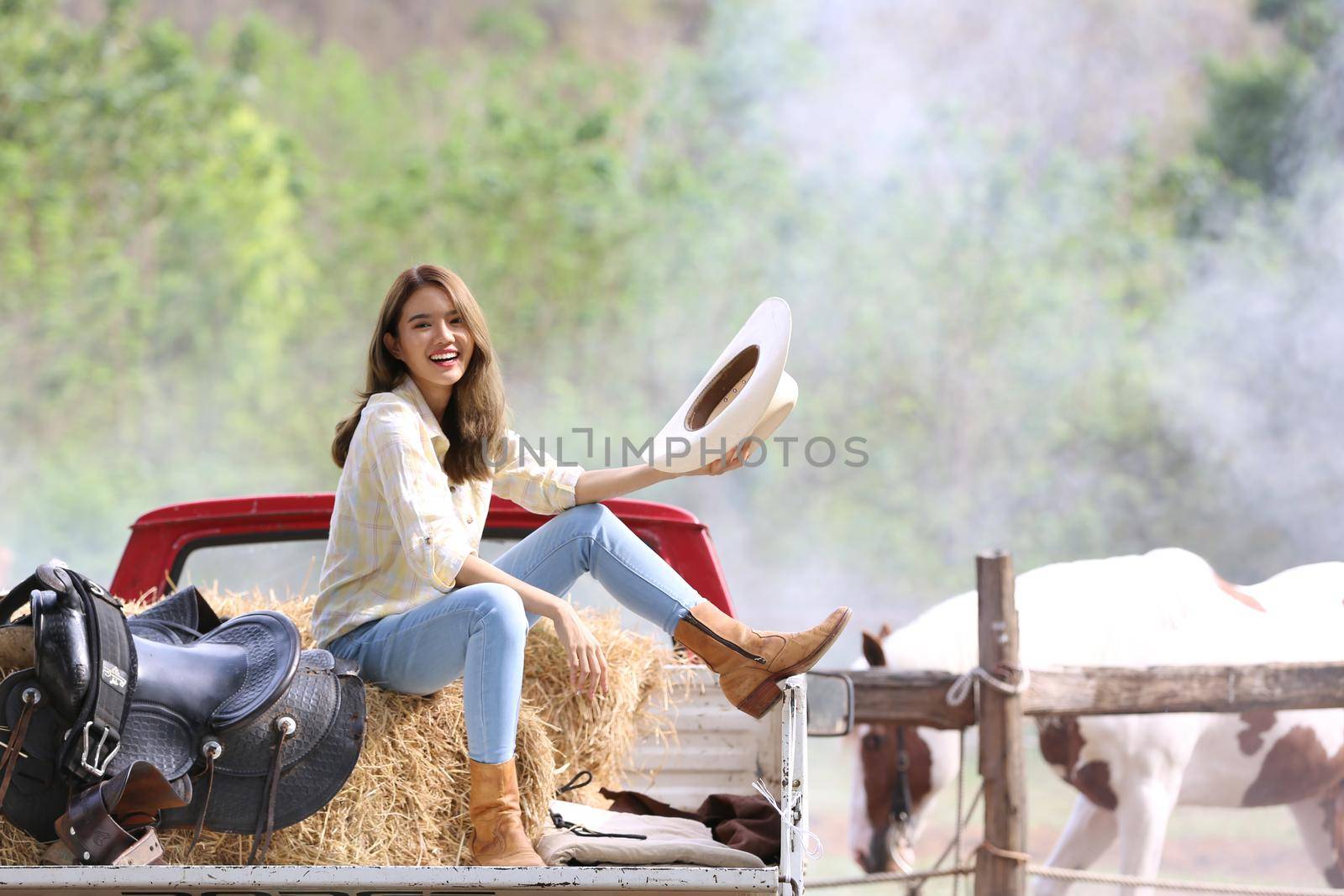 A woman in a cowgirl style sits in a horse ranch with a western farm environment.