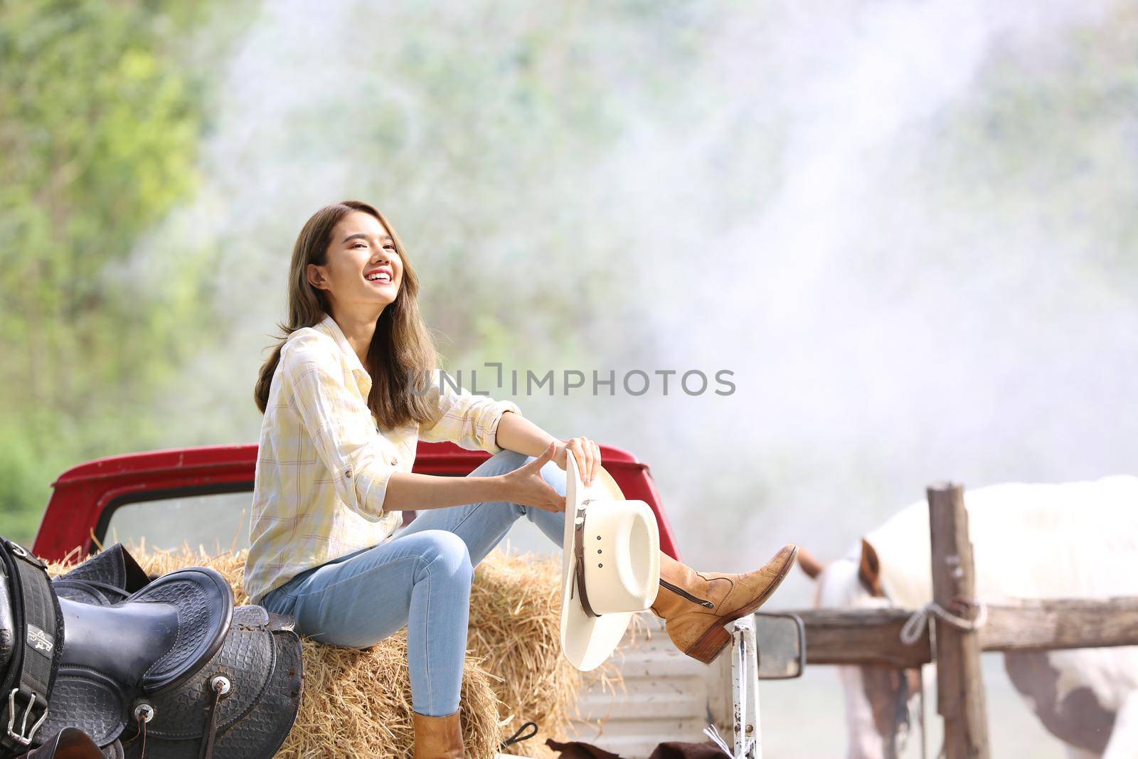 A woman in a cowgirl style sits in a horse ranch with a western farm environment.