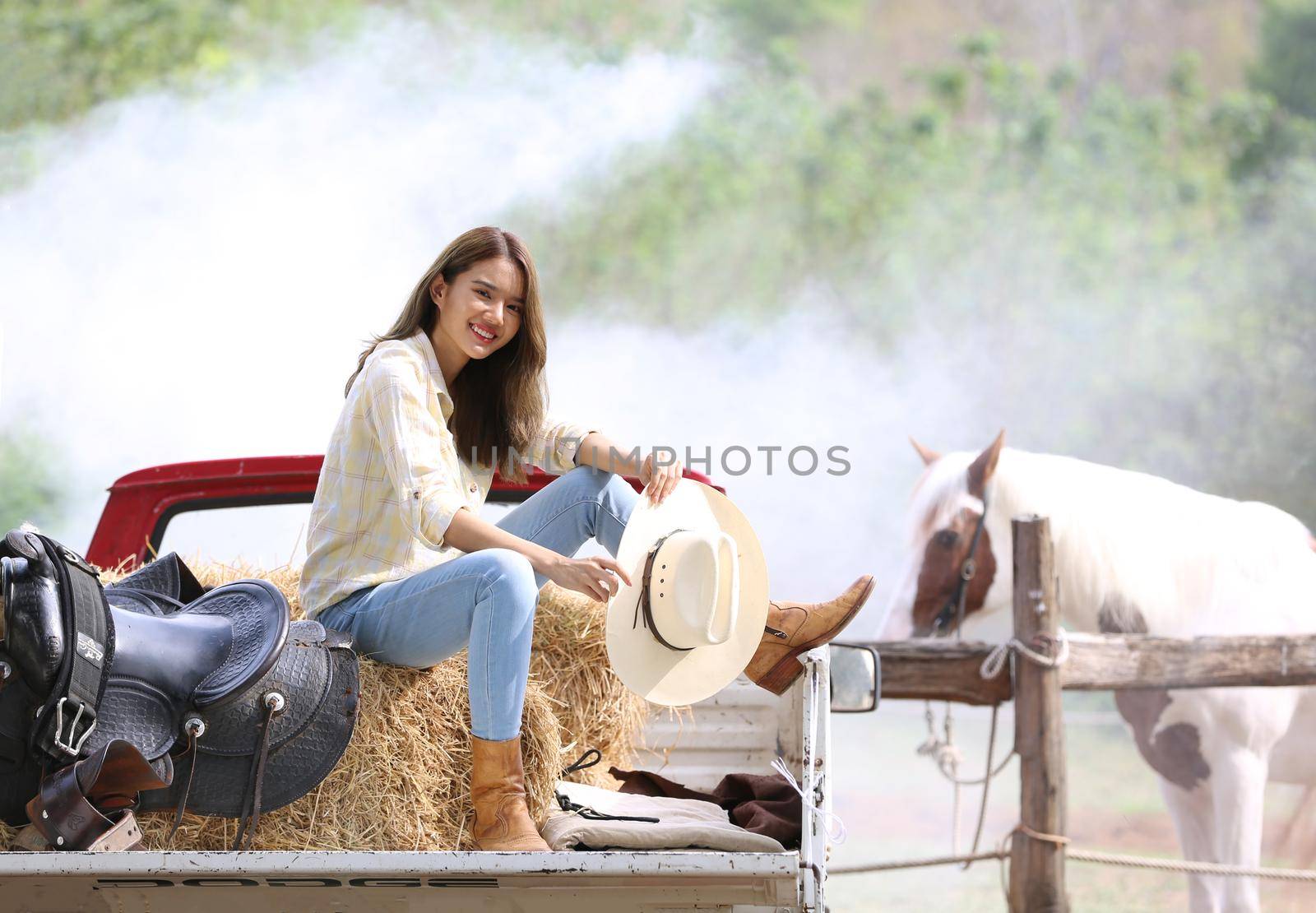 A woman in a cowgirl style sits in a horse ranch with a western farm environment.