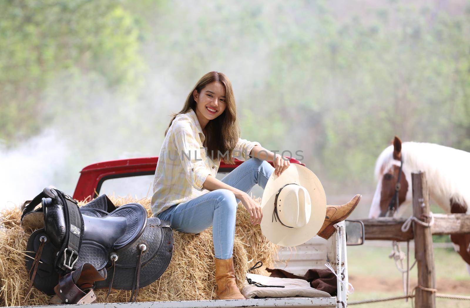 A woman in a cowgirl style sits in a horse ranch with a western farm environment.