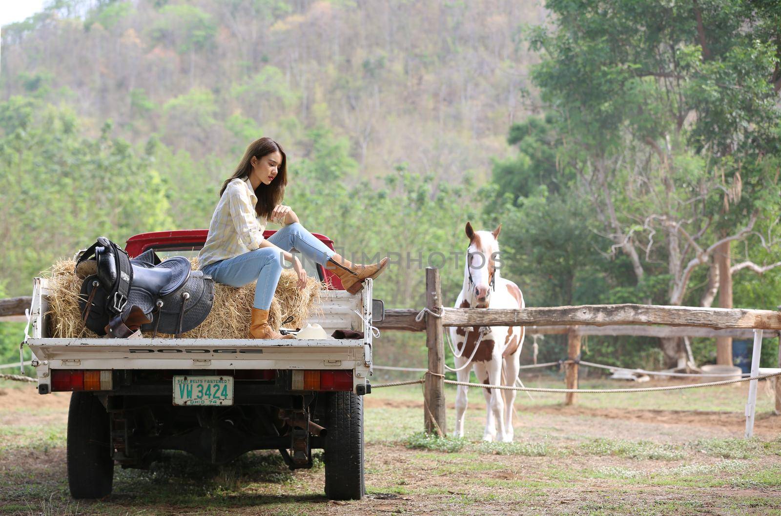 A woman in a cowgirl style sits in a horse ranch with a western farm environment.
