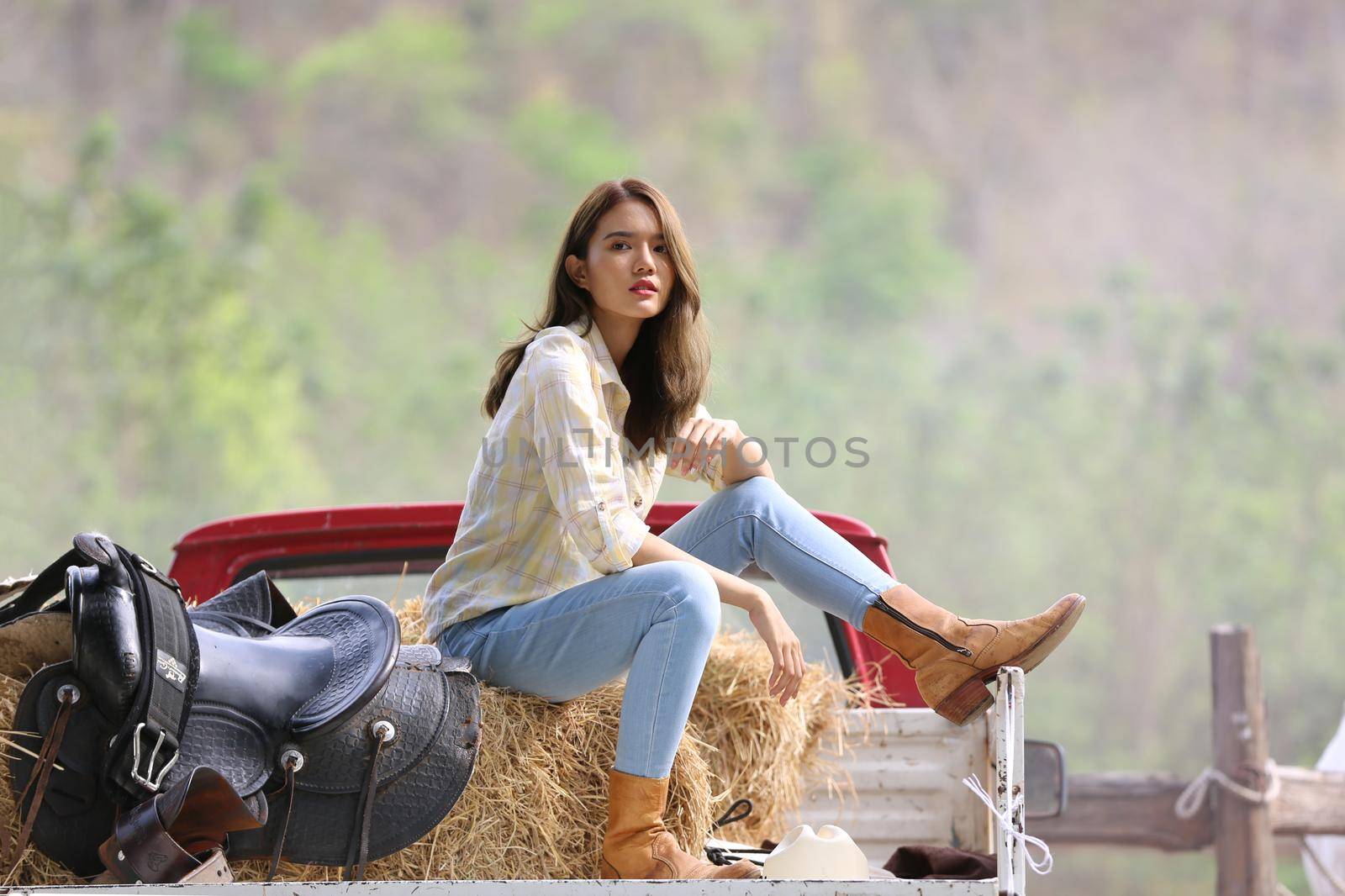 A woman in a cowgirl style sits in a horse ranch with a western farm environment.