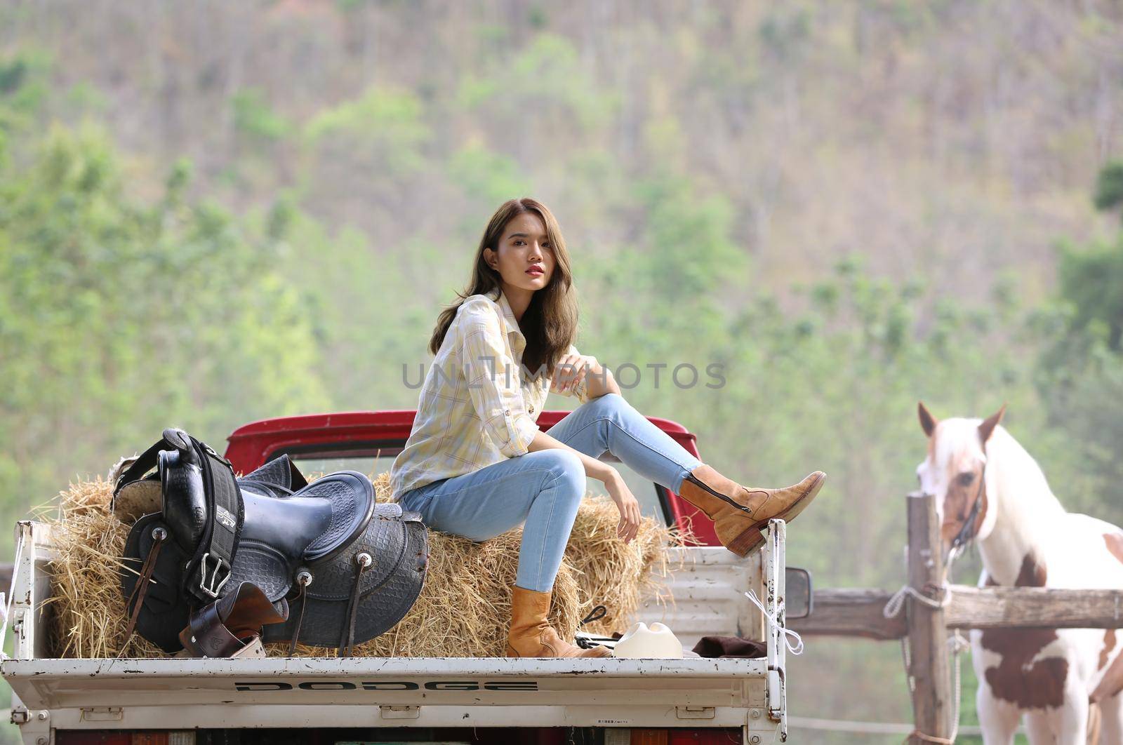 A woman in a cowgirl style sits in a horse ranch with a western farm environment.