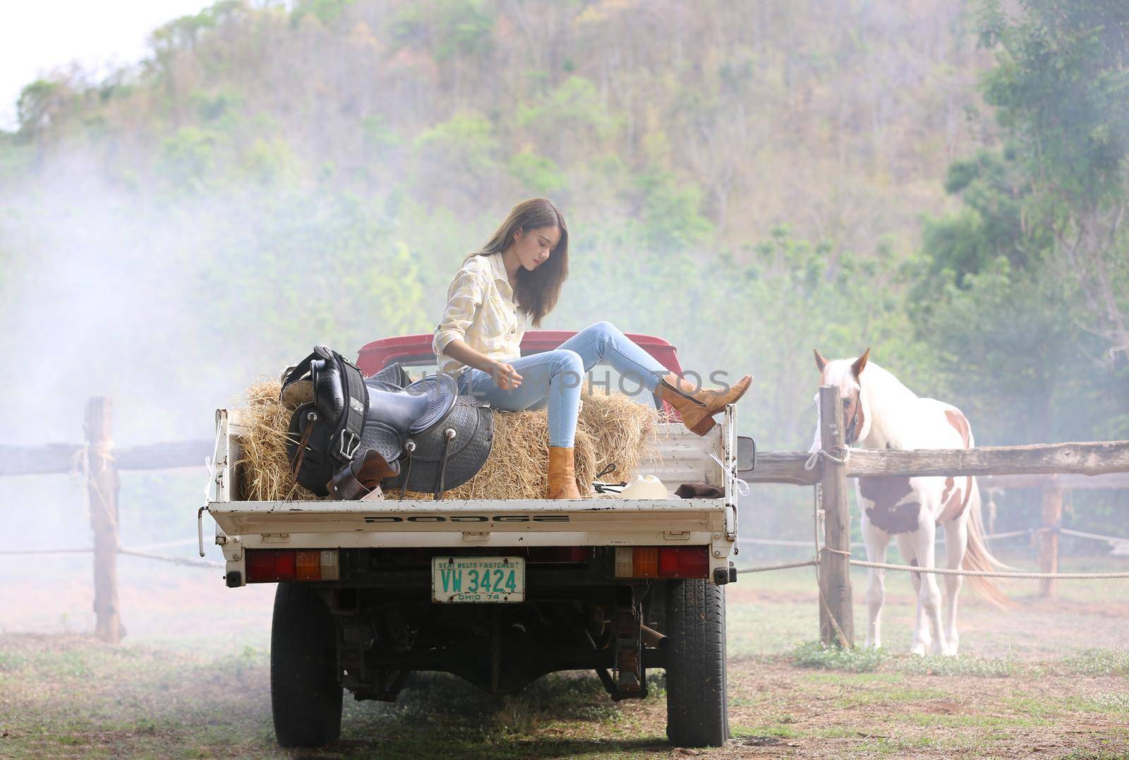 A woman in a cowgirl style sits in a horse ranch with a western farm environment.
