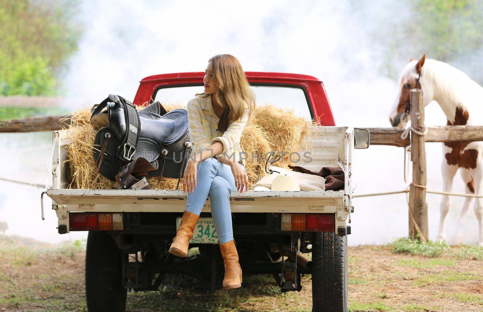 A woman in a cowgirl style sits in a horse ranch with a western farm environment.