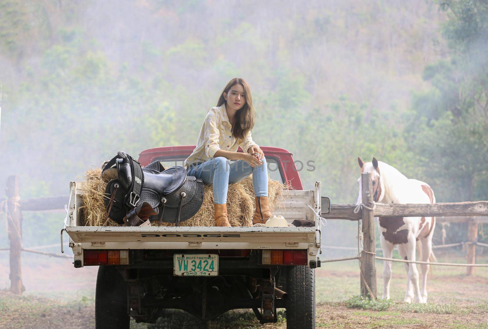 A woman in a cowgirl style sits in a horse ranch with a western farm environment.
