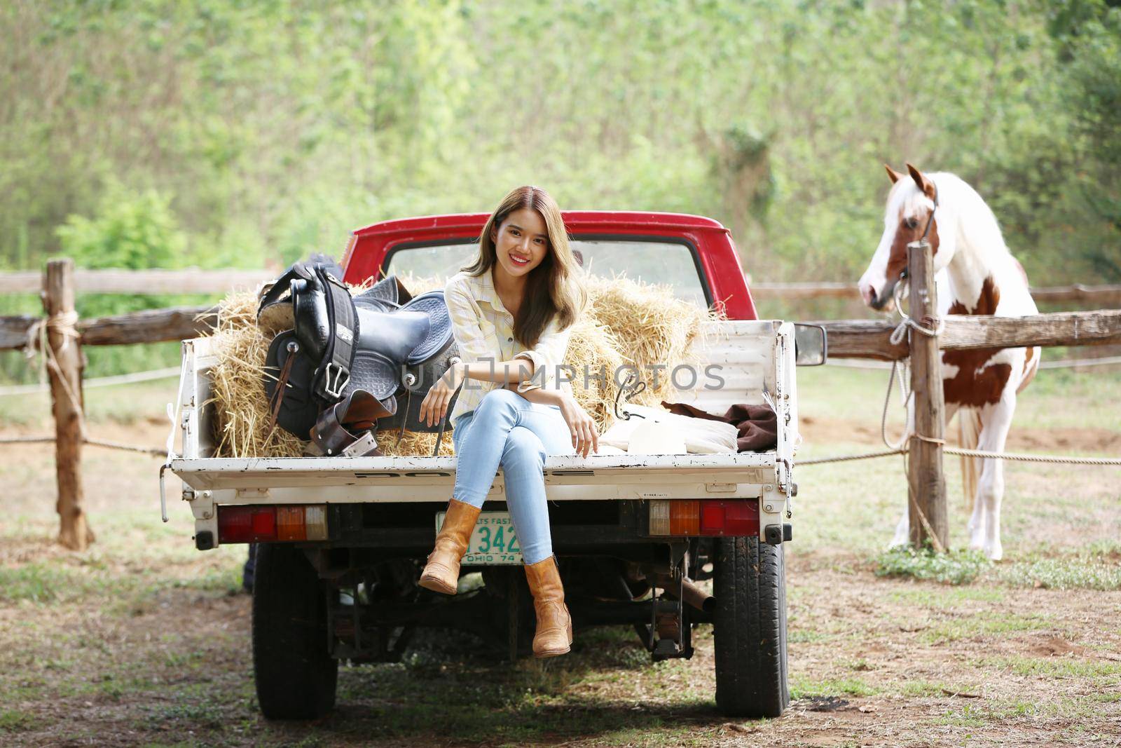 A woman in a cowgirl style sits in a horse ranch with a western farm environment.