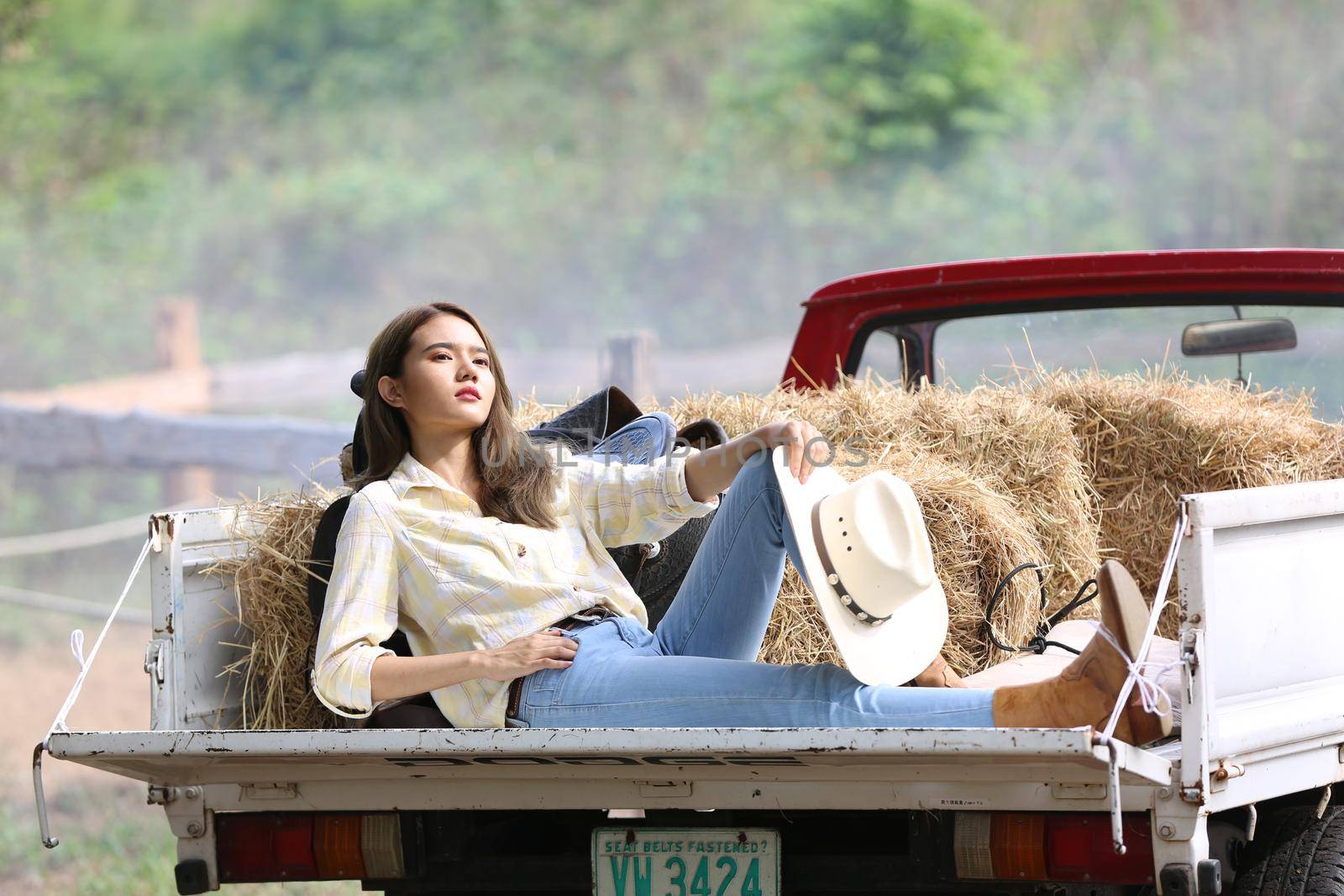 A woman in a cowgirl style sits in a horse ranch with a western farm environment.