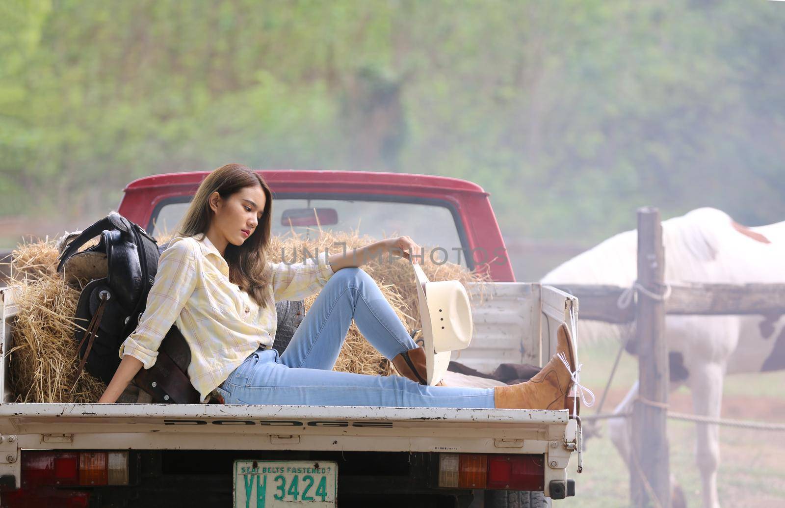 A woman in a cowgirl style sits in a horse ranch with a western farm environment.