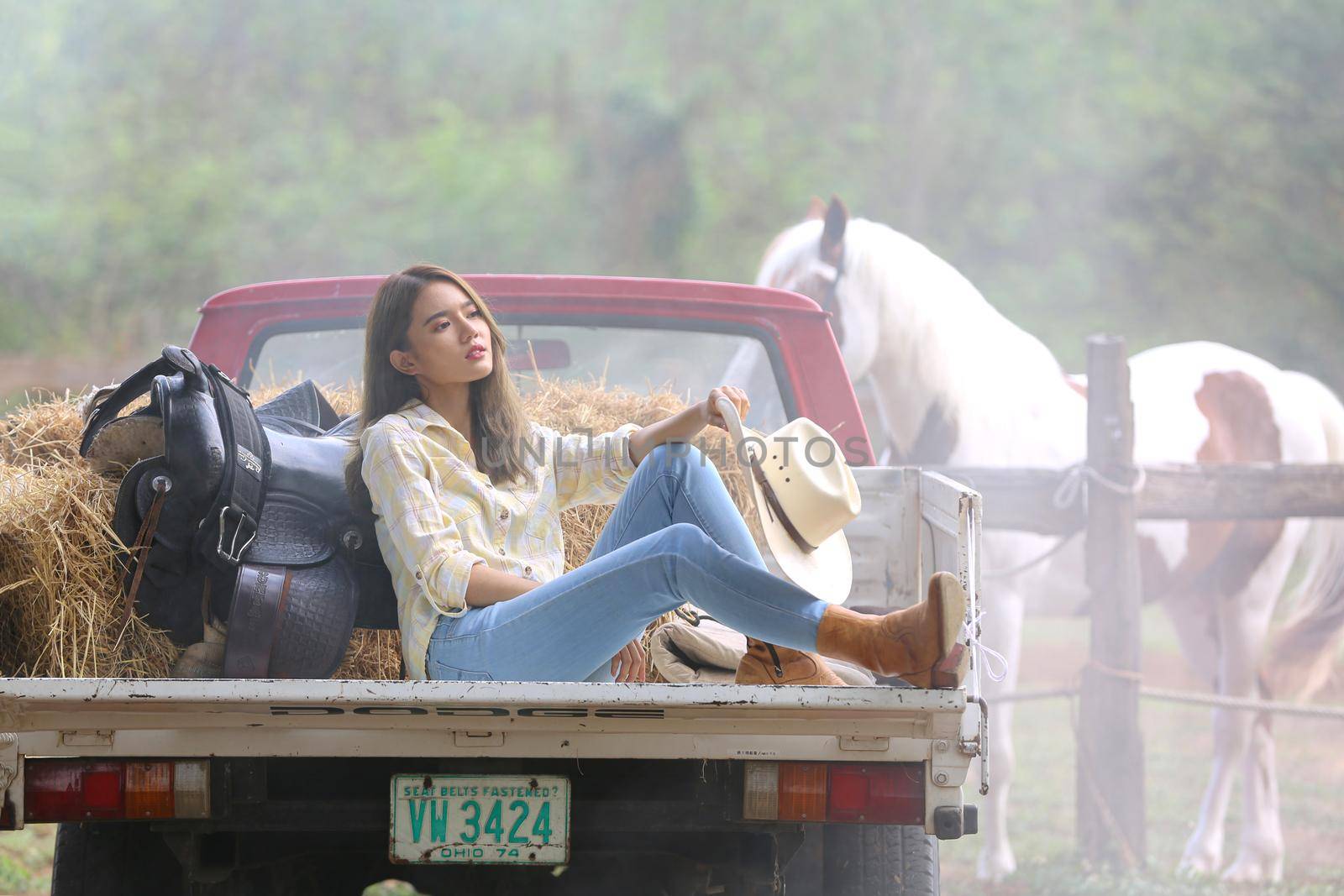 A woman in a cowgirl style sits in a horse ranch with a western farm environment.