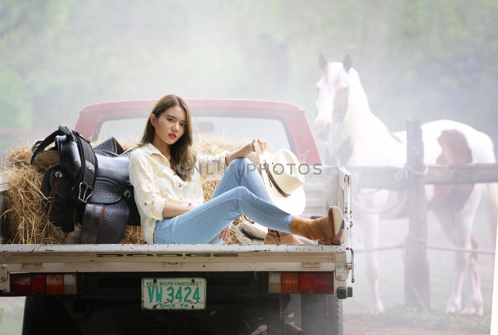 A woman in a cowgirl style sits in a horse ranch with a western farm environment.