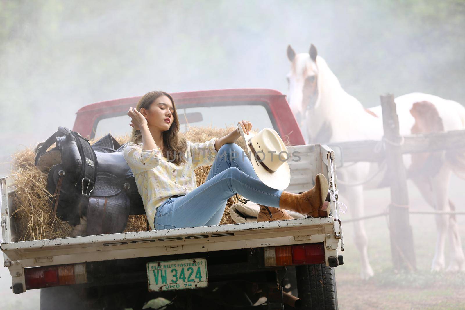 A woman in a cowgirl style sits in a horse ranch with a western farm environment.