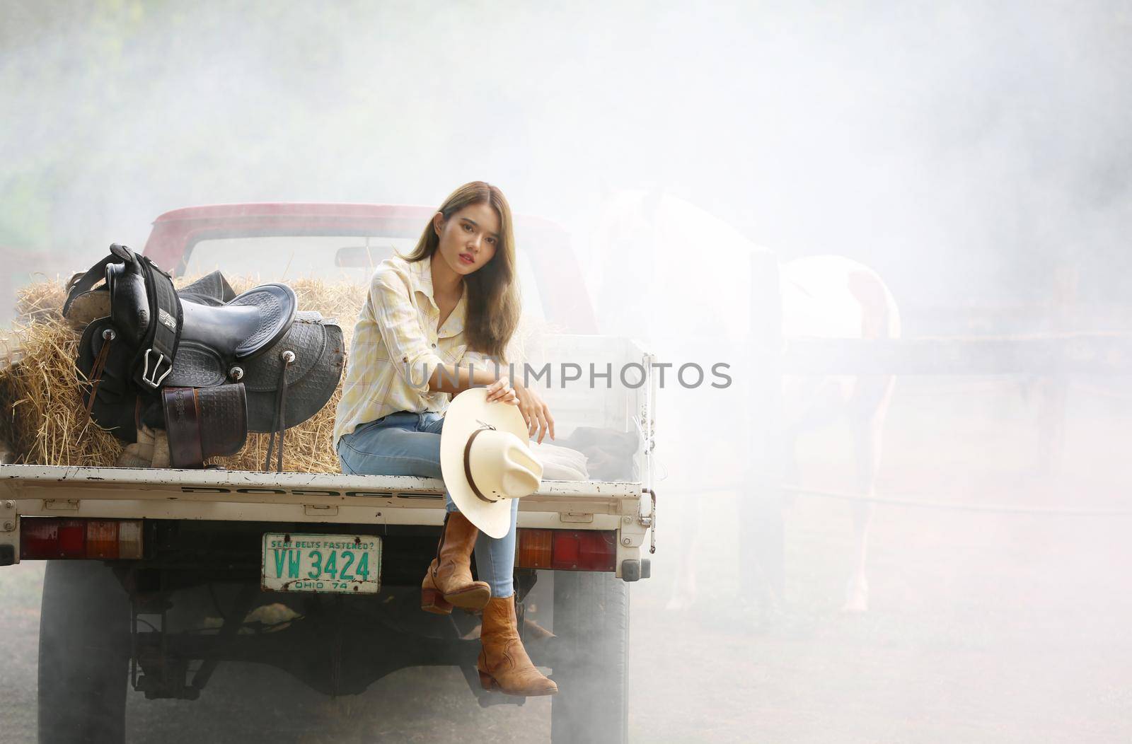 A woman in a cowgirl style sits in a horse ranch with a western farm environment.