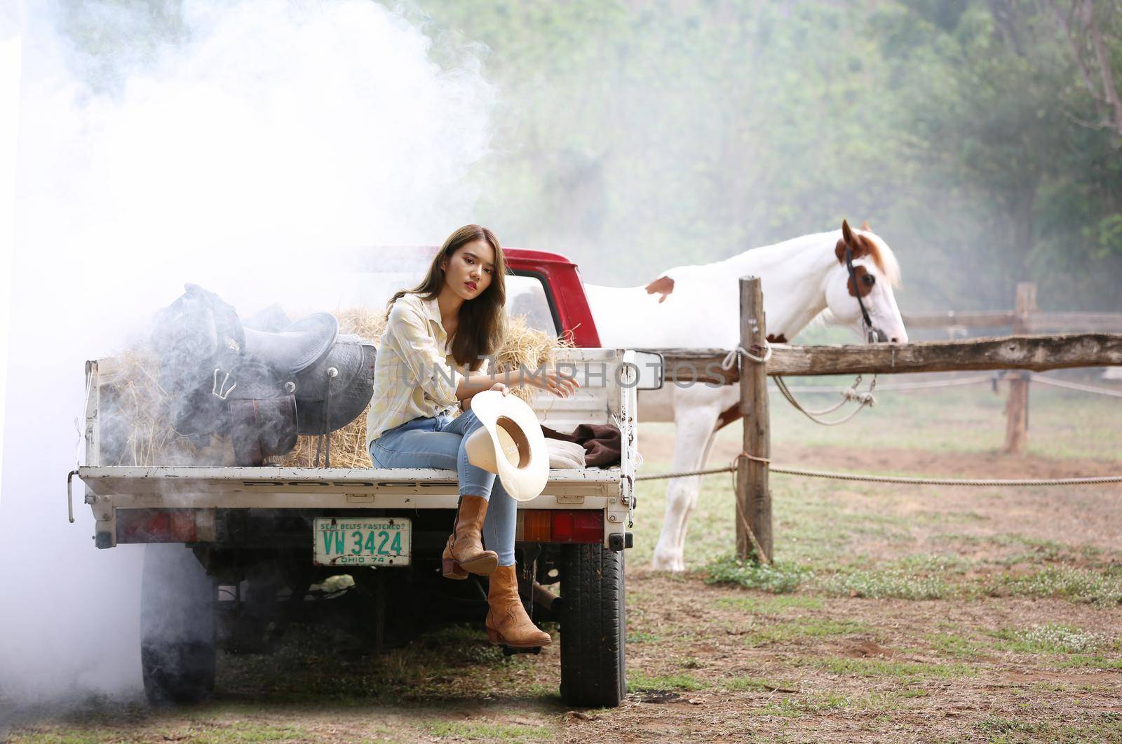A woman in a cowgirl style sits in a horse ranch with a western farm environment.