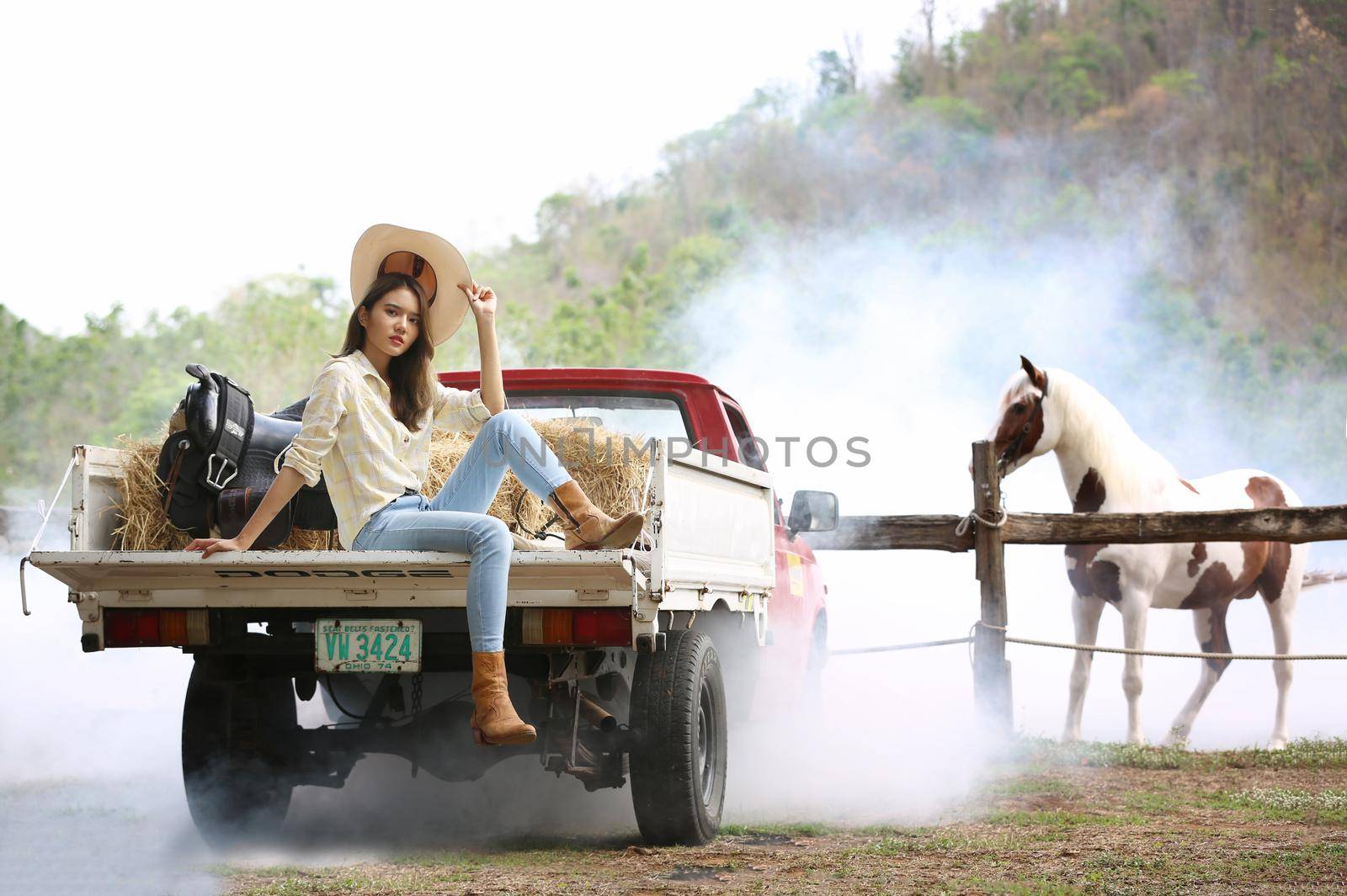A woman in a cowgirl style sits in a horse ranch with a western farm environment.