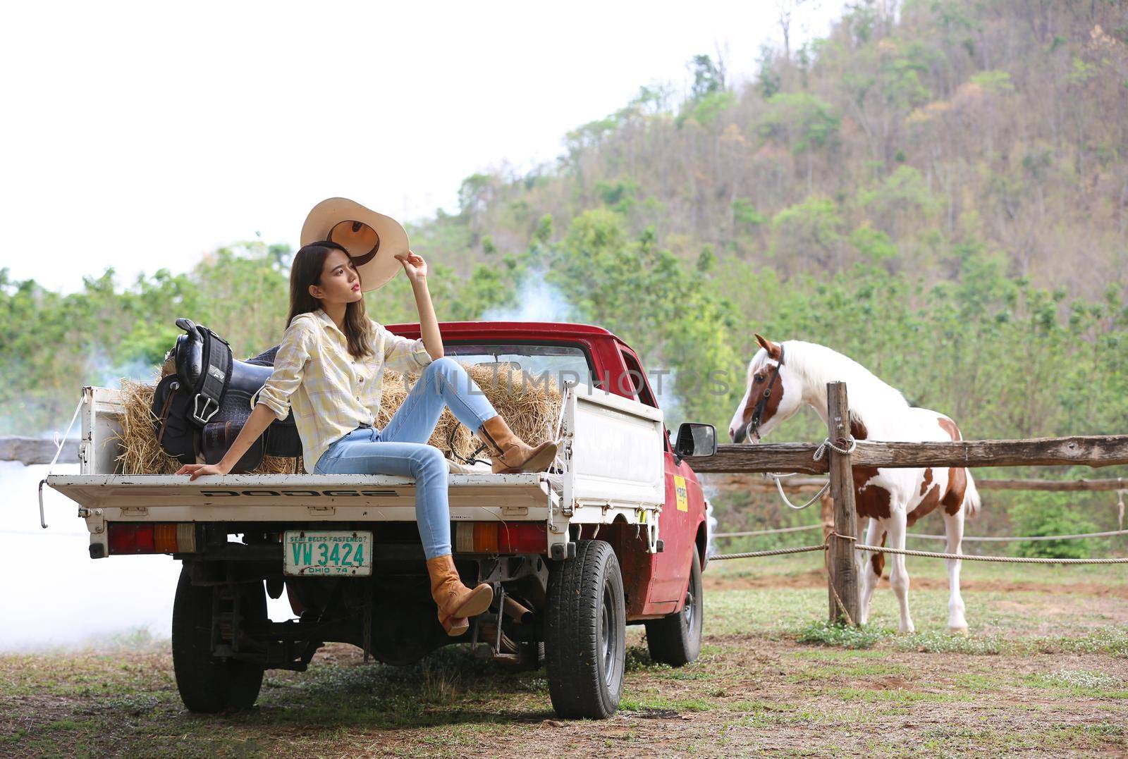 A woman in a cowgirl style sits in a horse ranch with a western farm environment.