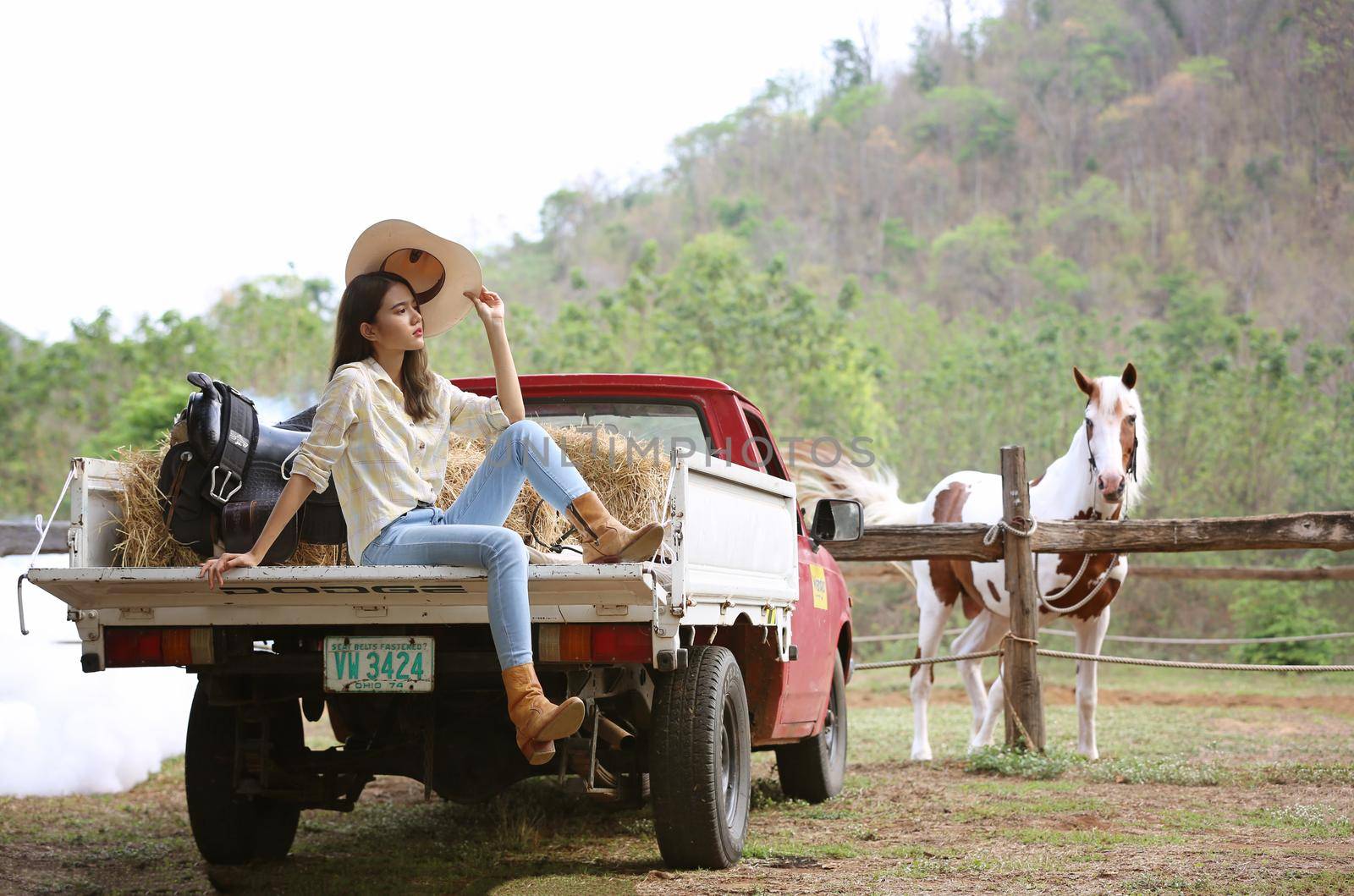 A woman in a cowgirl style sits in a horse ranch with a western farm environment.