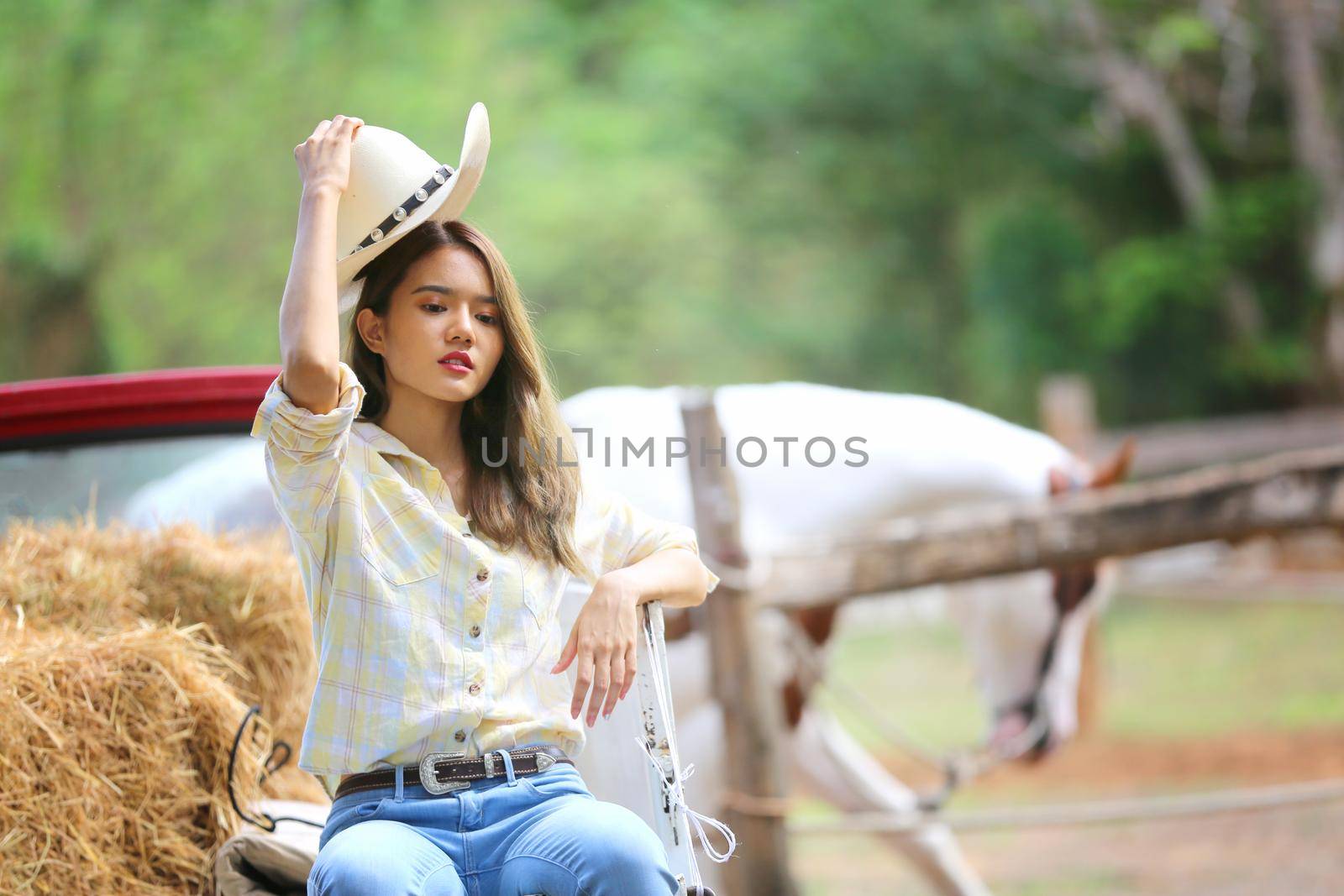 A woman in a cowgirl style sits in a horse ranch with a western farm environment.