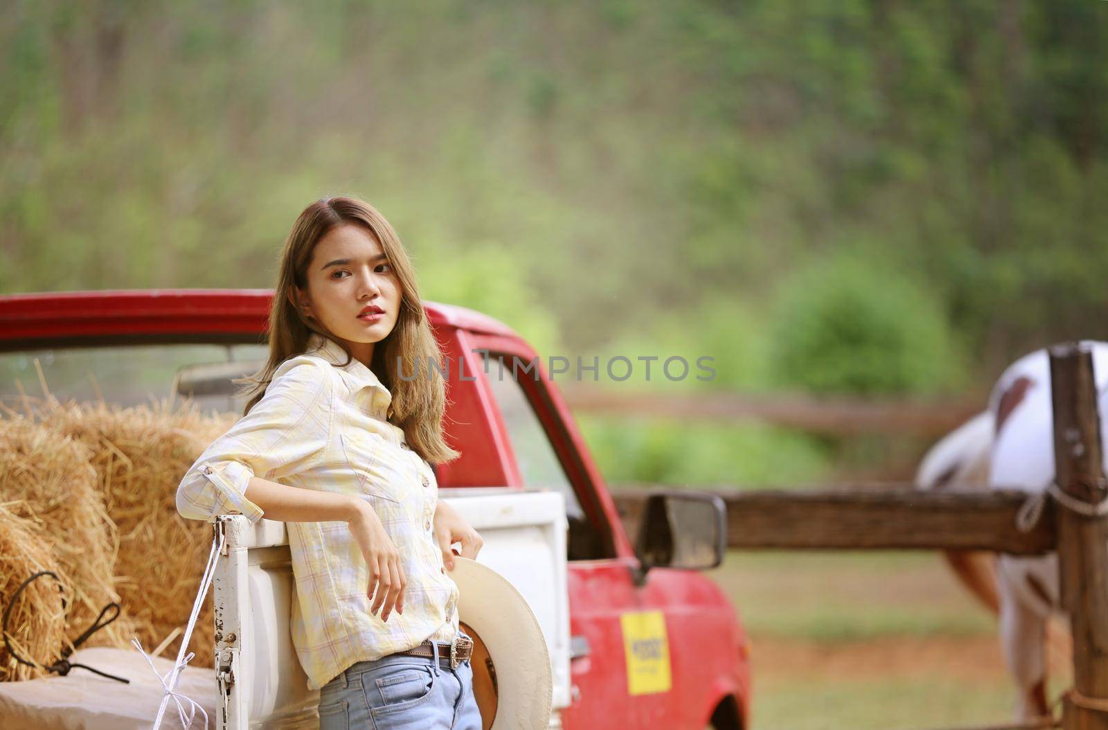 A woman in a cowgirl style sits in a horse ranch with a western farm environment.