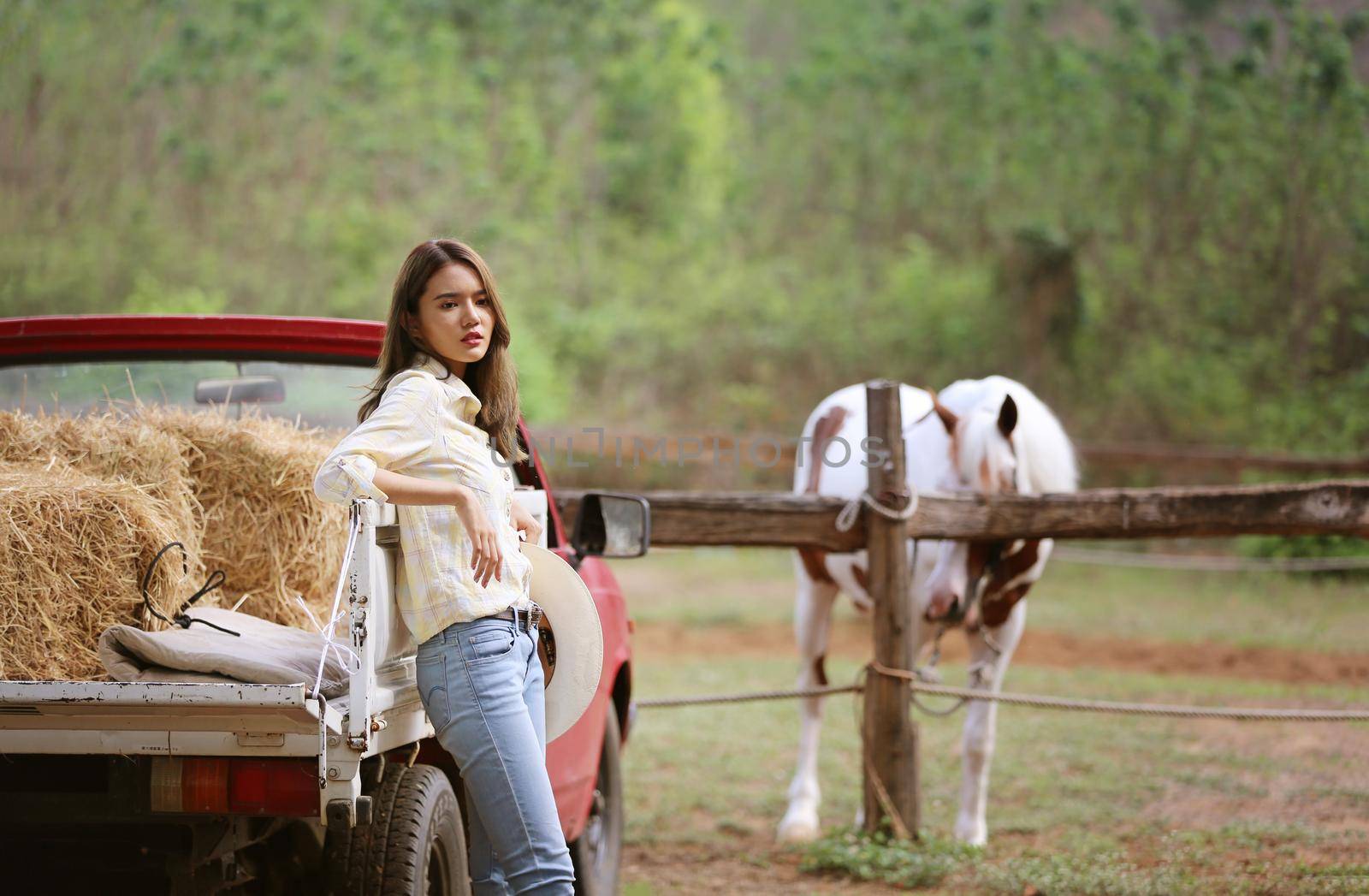 A woman in a cowgirl style sits in a horse ranch with a western farm environment.