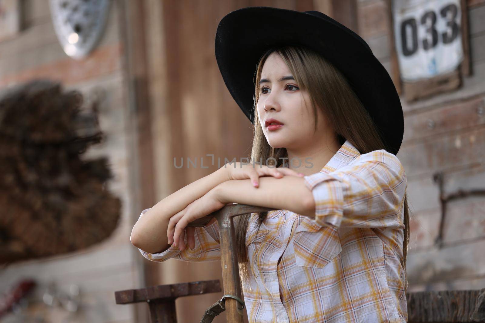 A woman in a cowgirl style sits in a horse ranch with a western farm environment.