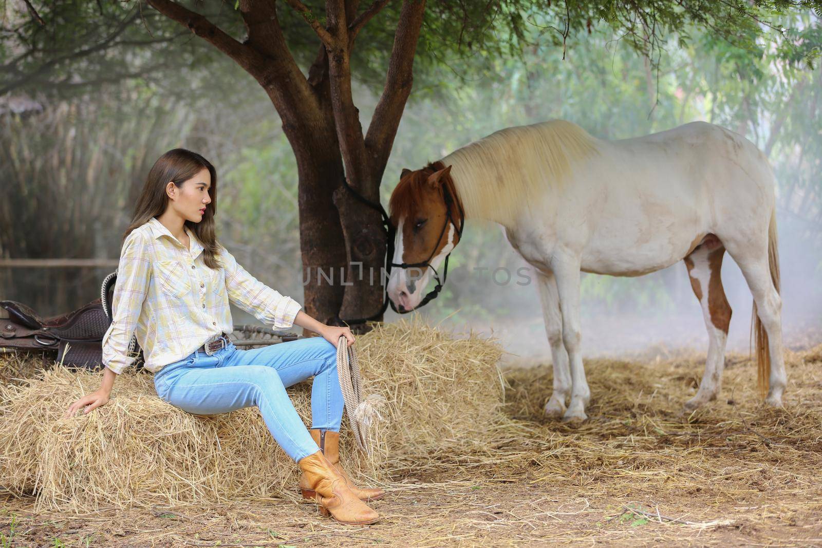 A woman in a cowgirl style sits in a horse ranch with a western farm environment.