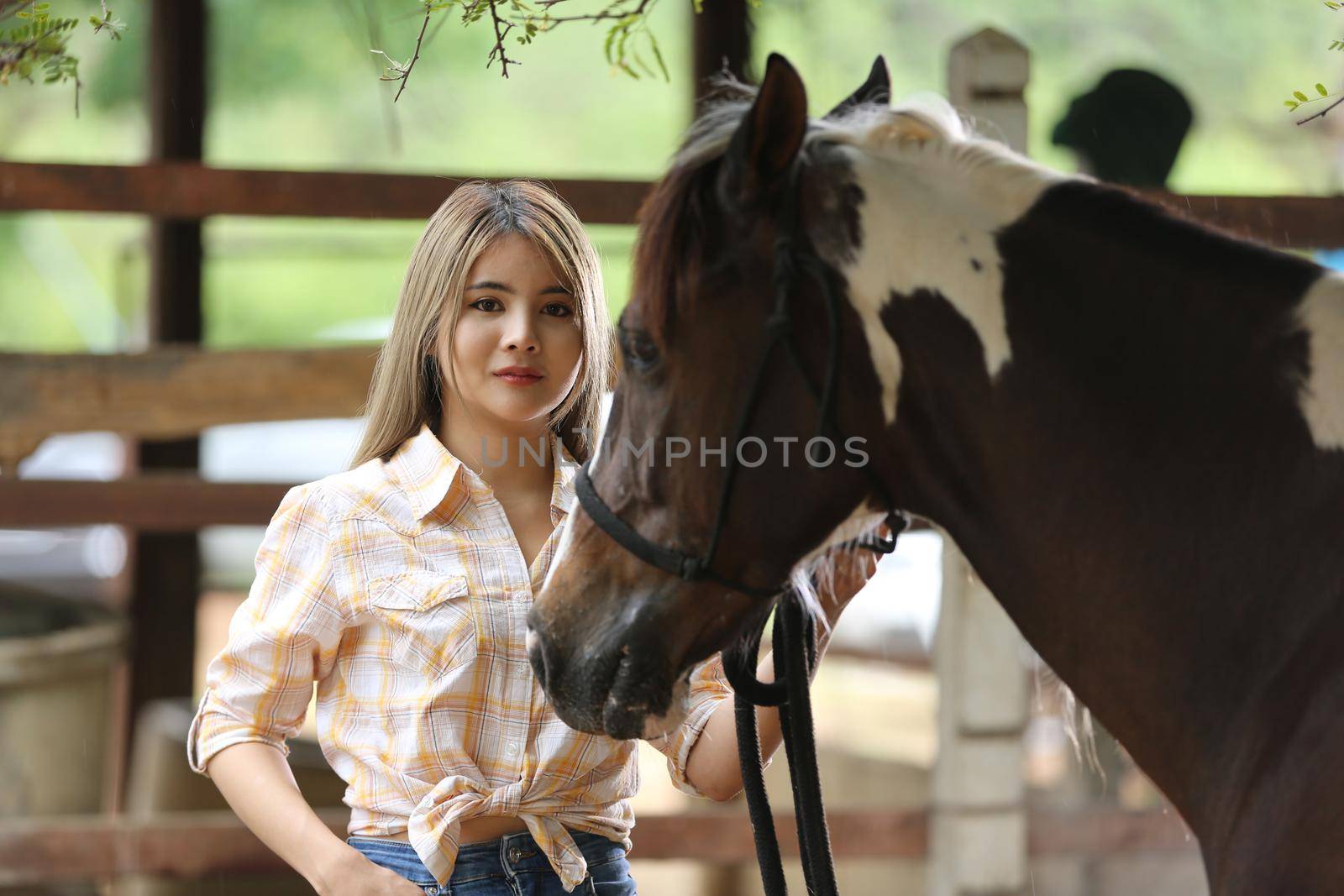 A woman in a cowgirl style sits in a horse ranch with a western farm environment.