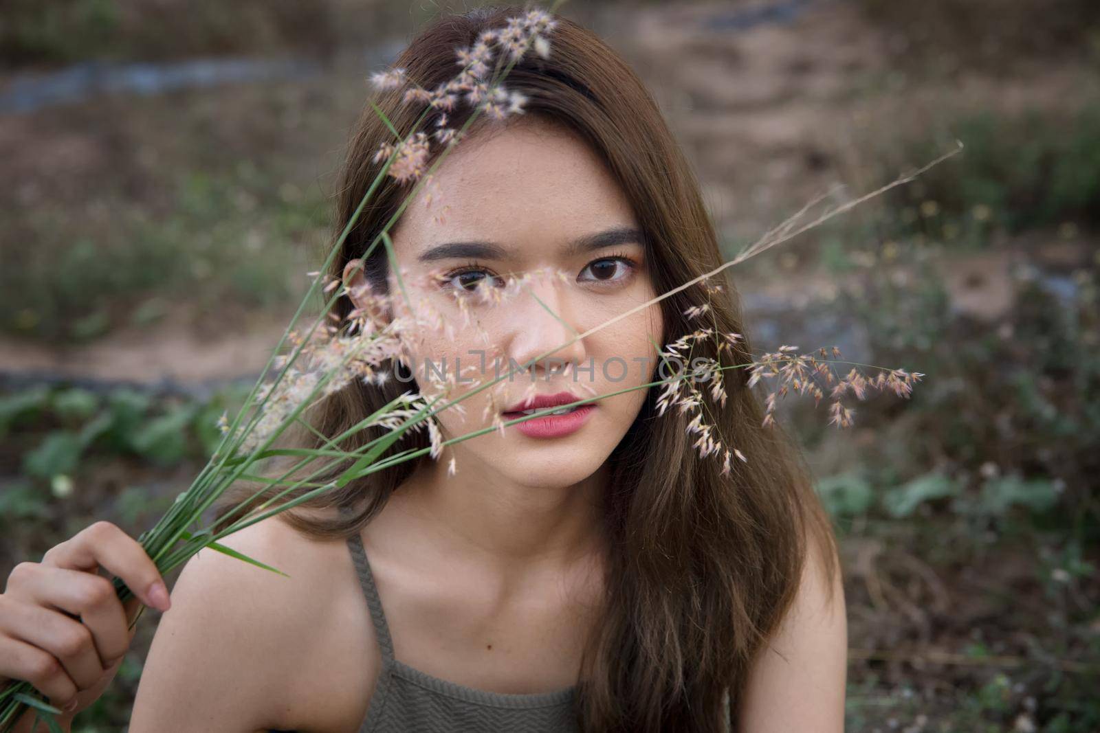 A beautiful woman with long hair in a dress sitting on a meadow and flowers in the evening light.
