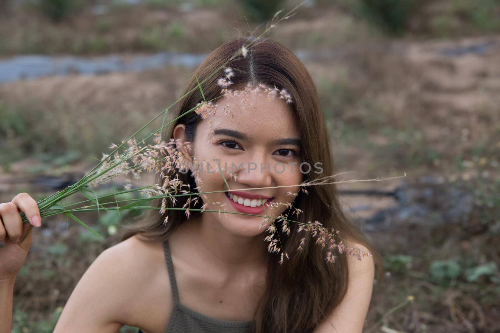 A beautiful woman with long hair in a dress sitting on a meadow and flowers in the evening light.