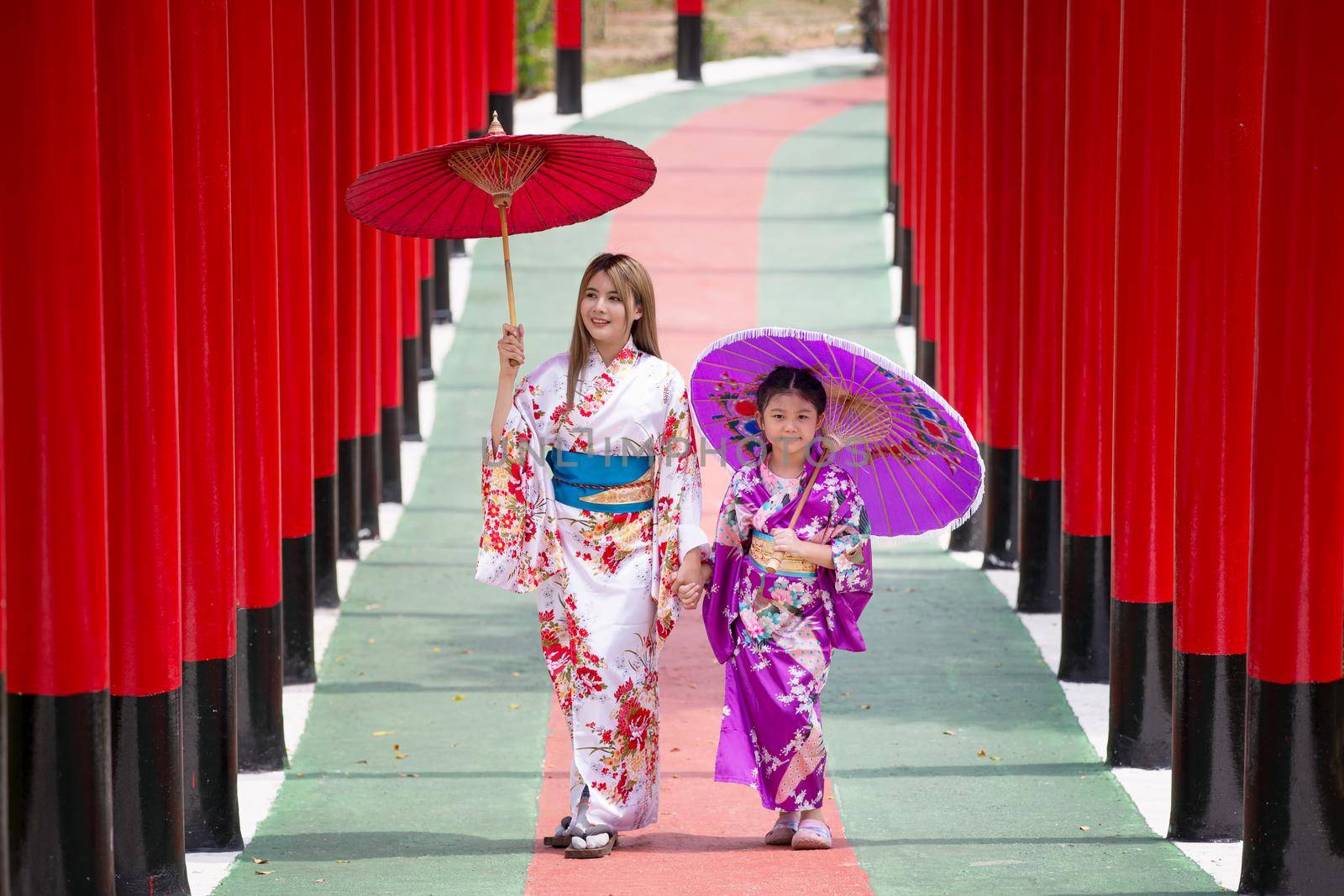  woman and little girl in kimono holding umbrella walking into at the shrine red gate, in Japanese garden. by chuanchai