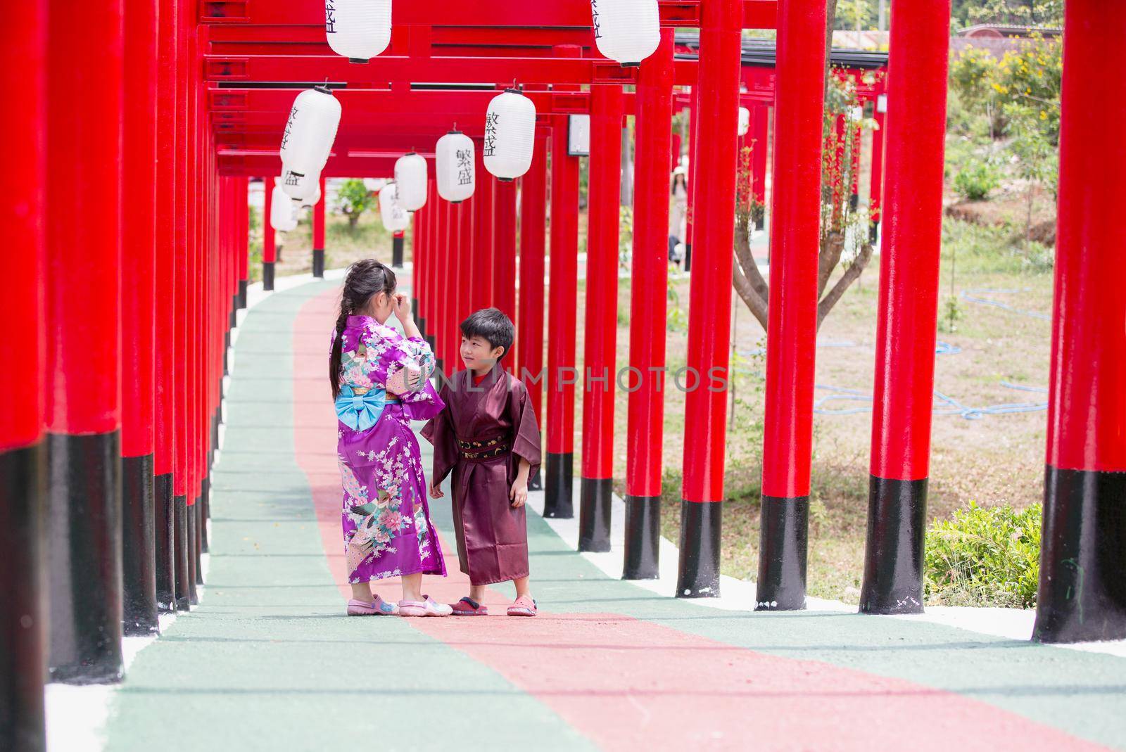 Two kids in kimono walking into at the shrine red gate, in Japanese garden. by chuanchai