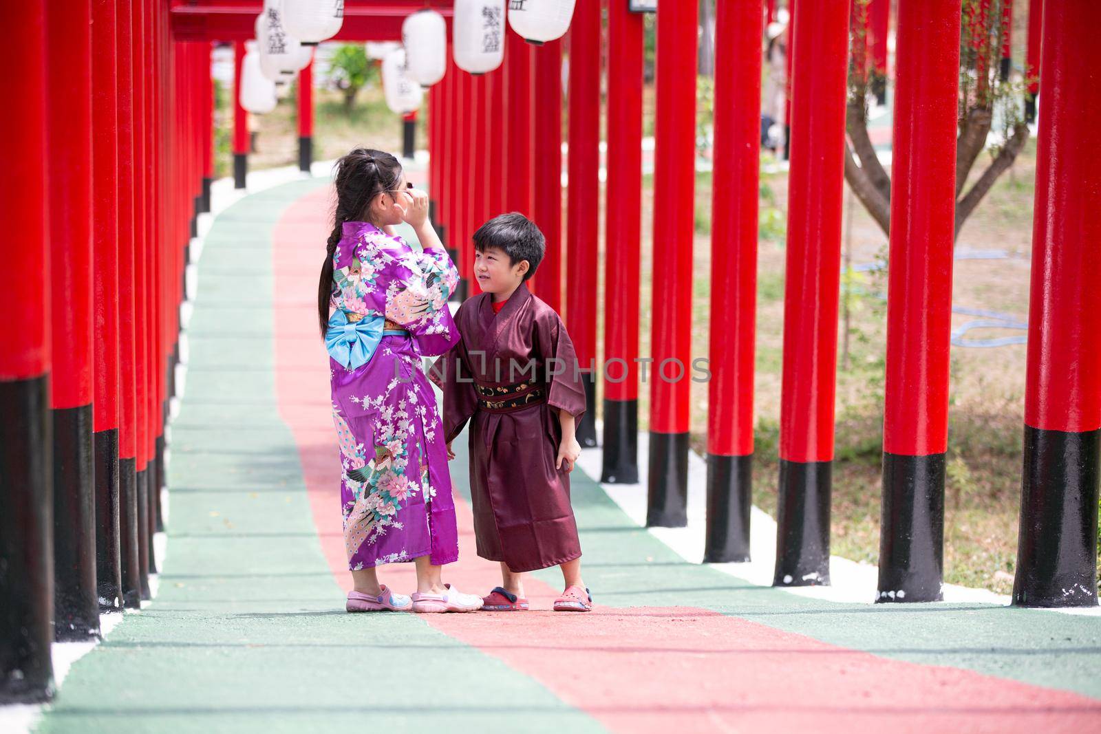 Two kids in kimono walking into at the shrine red gate, in Japanese garden. by chuanchai