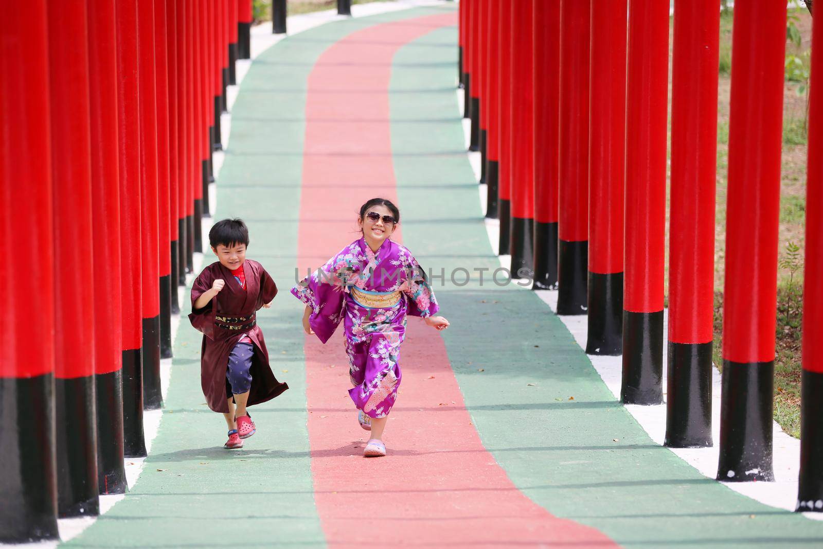 Two kids in kimono walking into at the shrine red gate, in Japanese garden.
