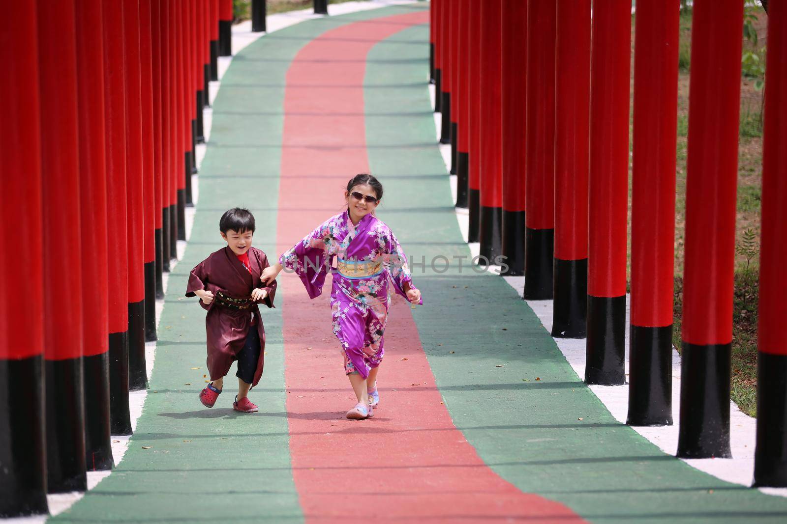 Two kids in kimono walking into at the shrine red gate, in Japanese garden.