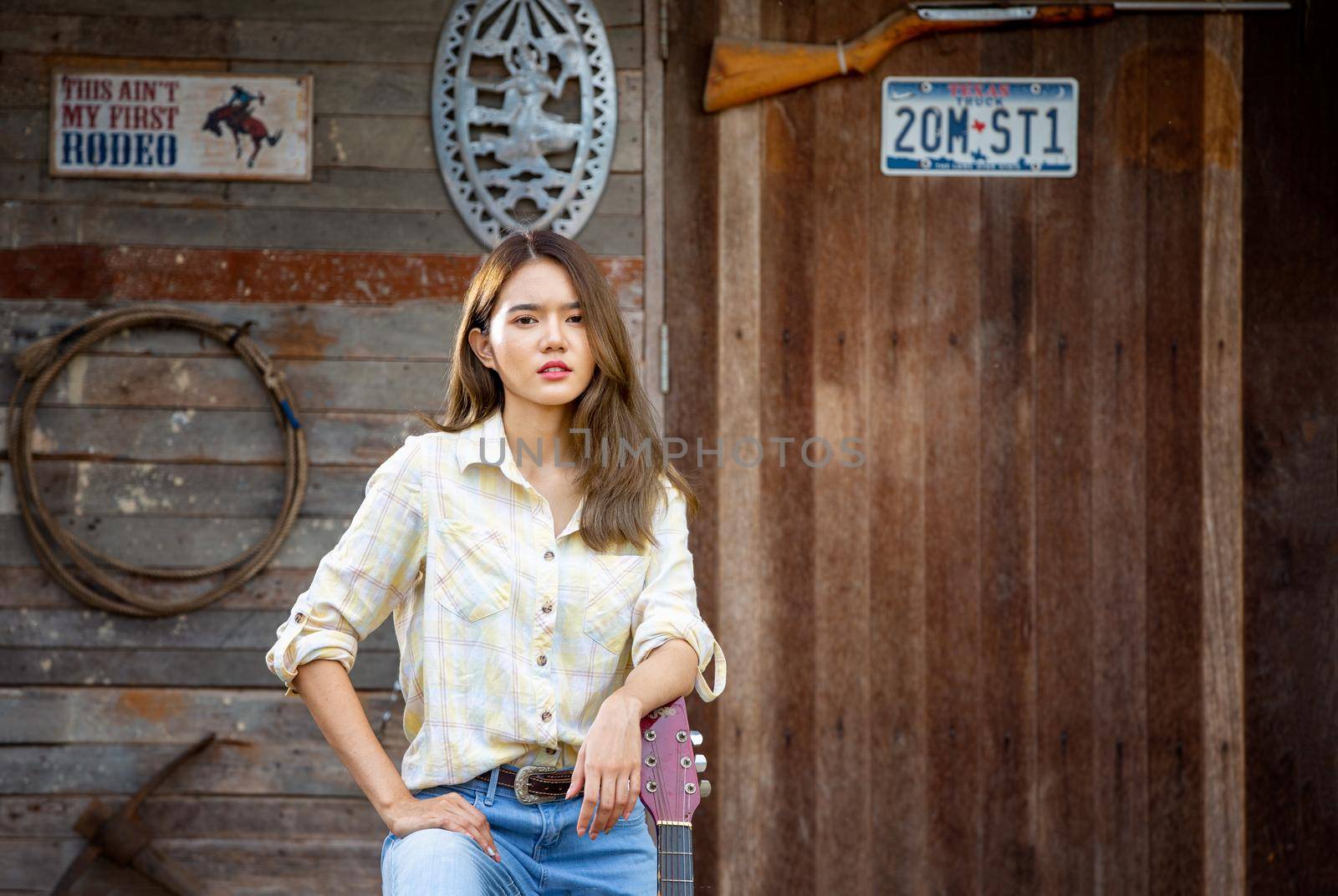 A woman in a cowgirl style sits in a horse ranch with a western farm environment.