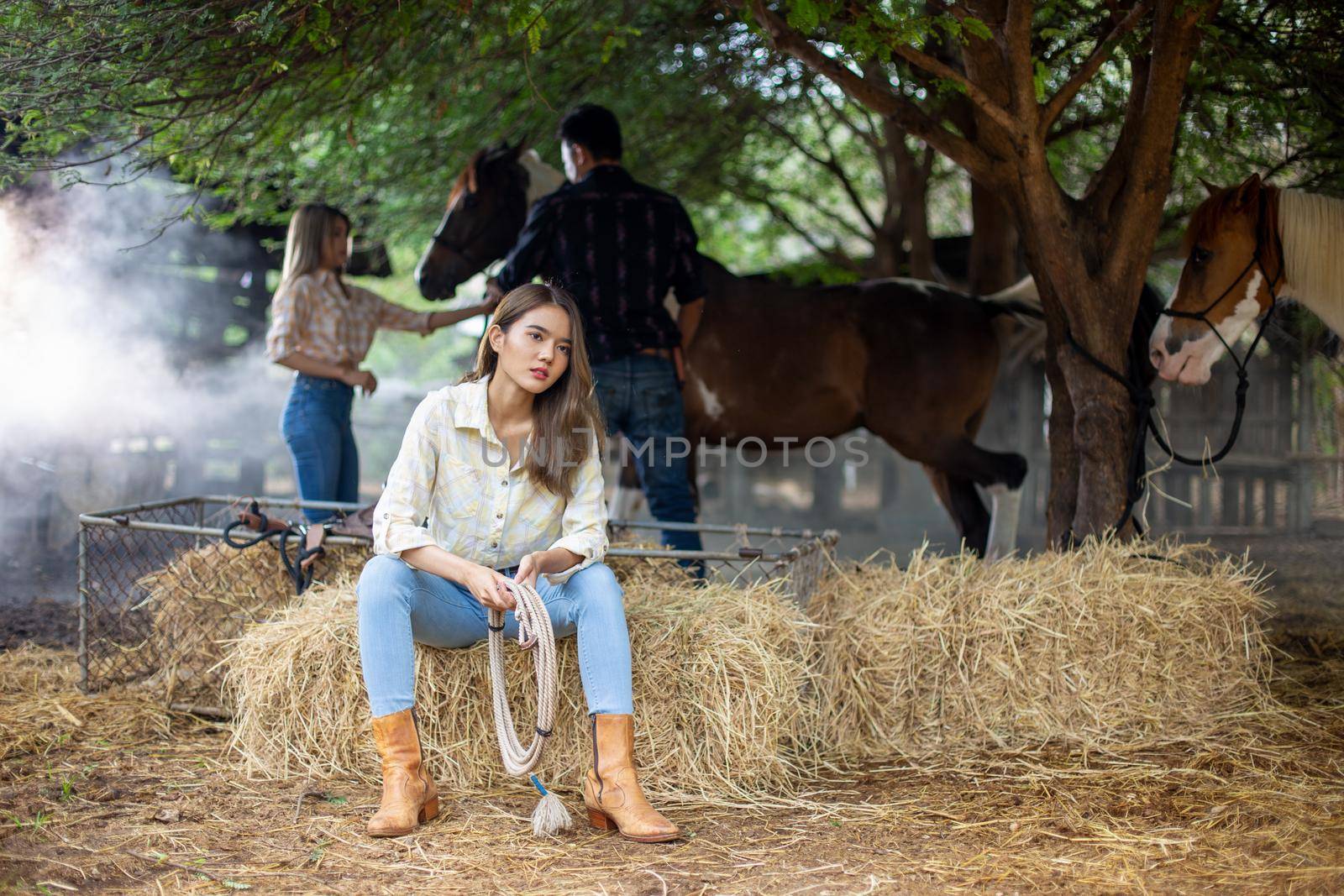 A woman in a cowgirl style sits in a horse ranch with a western farm environment.