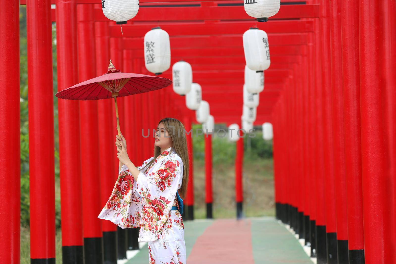 woman in kimono holding umbrella walking into at the shrine red gate, in Japanese garden.