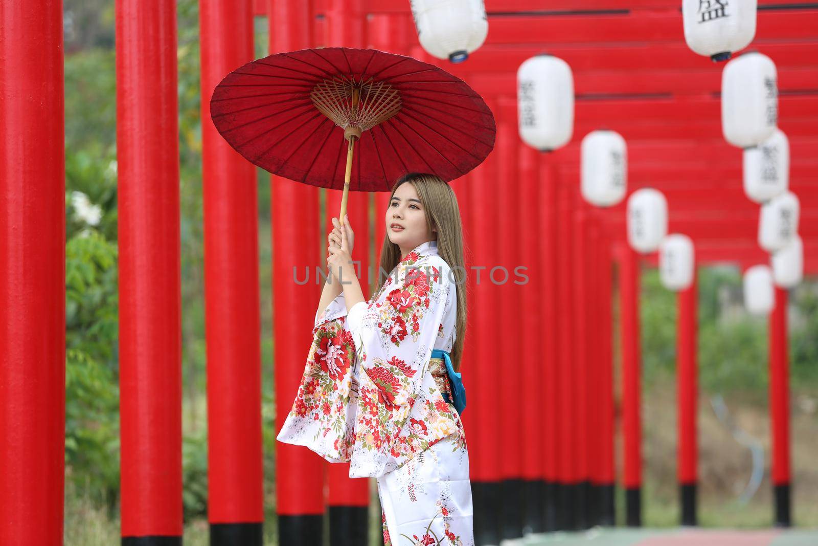 woman in kimono holding umbrella walking into at the shrine red gate, in Japanese garden.