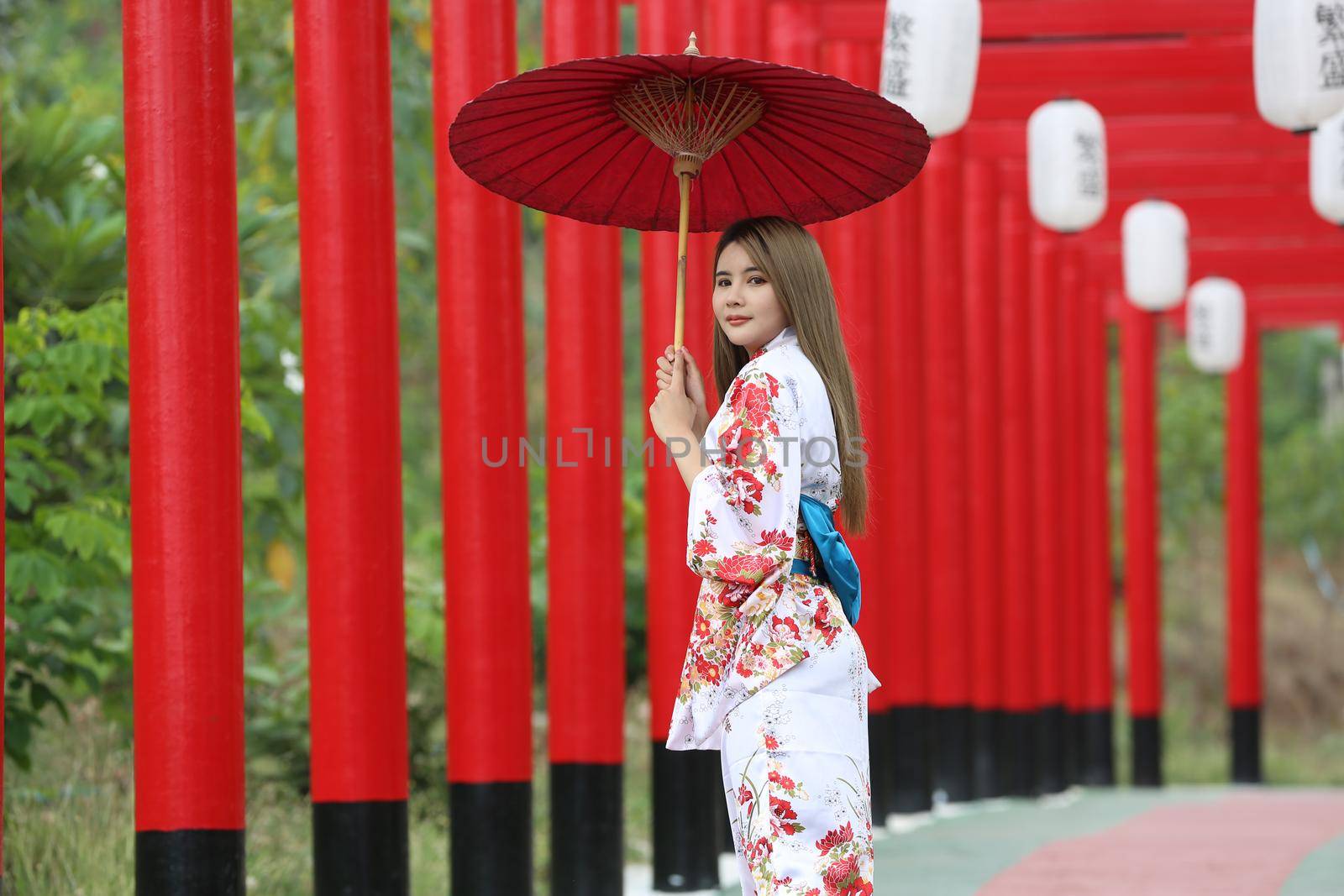 woman in kimono holding umbrella walking into at the shrine red gate, in Japanese garden.