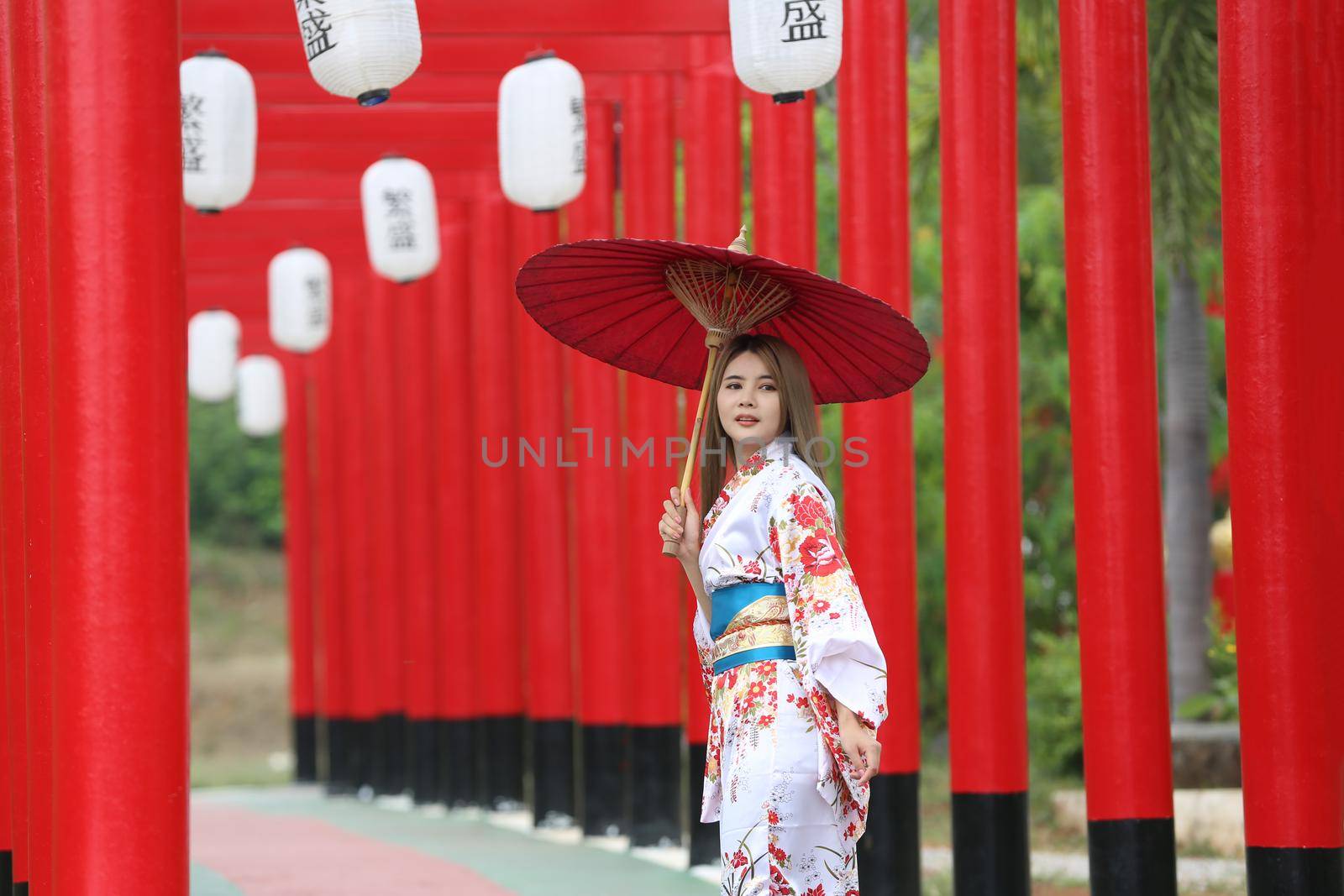 woman in kimono holding umbrella walking into at the shrine red gate, in Japanese garden.