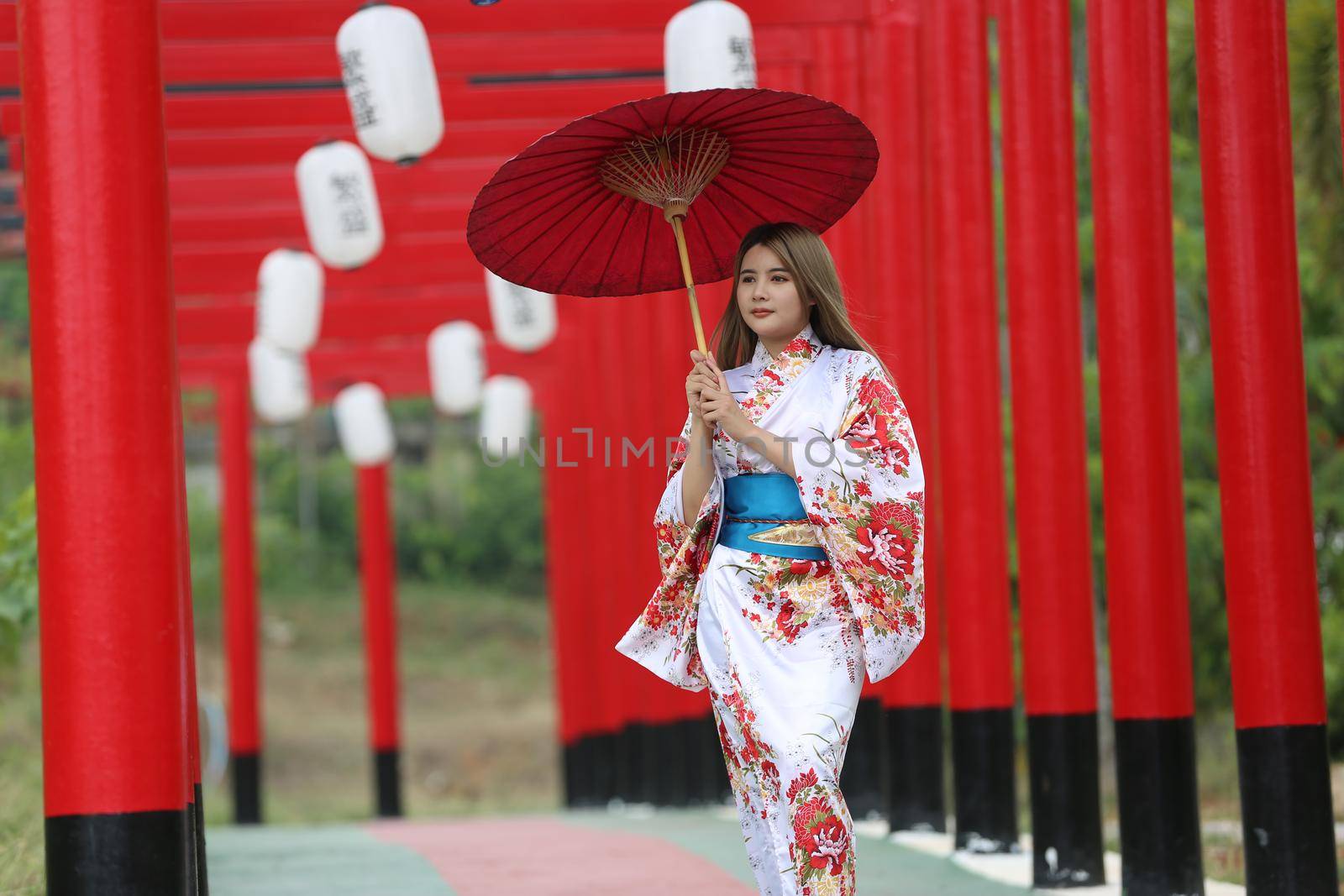 woman in kimono holding umbrella walking into at the shrine red gate, in Japanese garden.