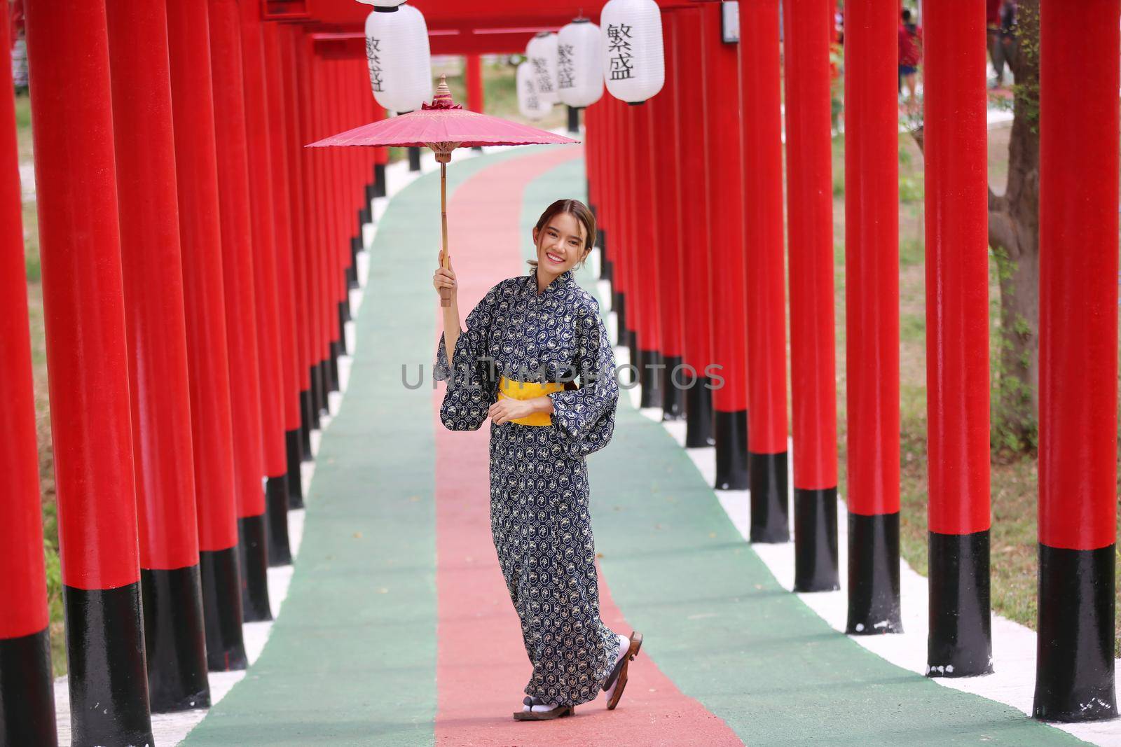 woman in kimono holding umbrella walking into at the shrine red gate, in Japanese garden.