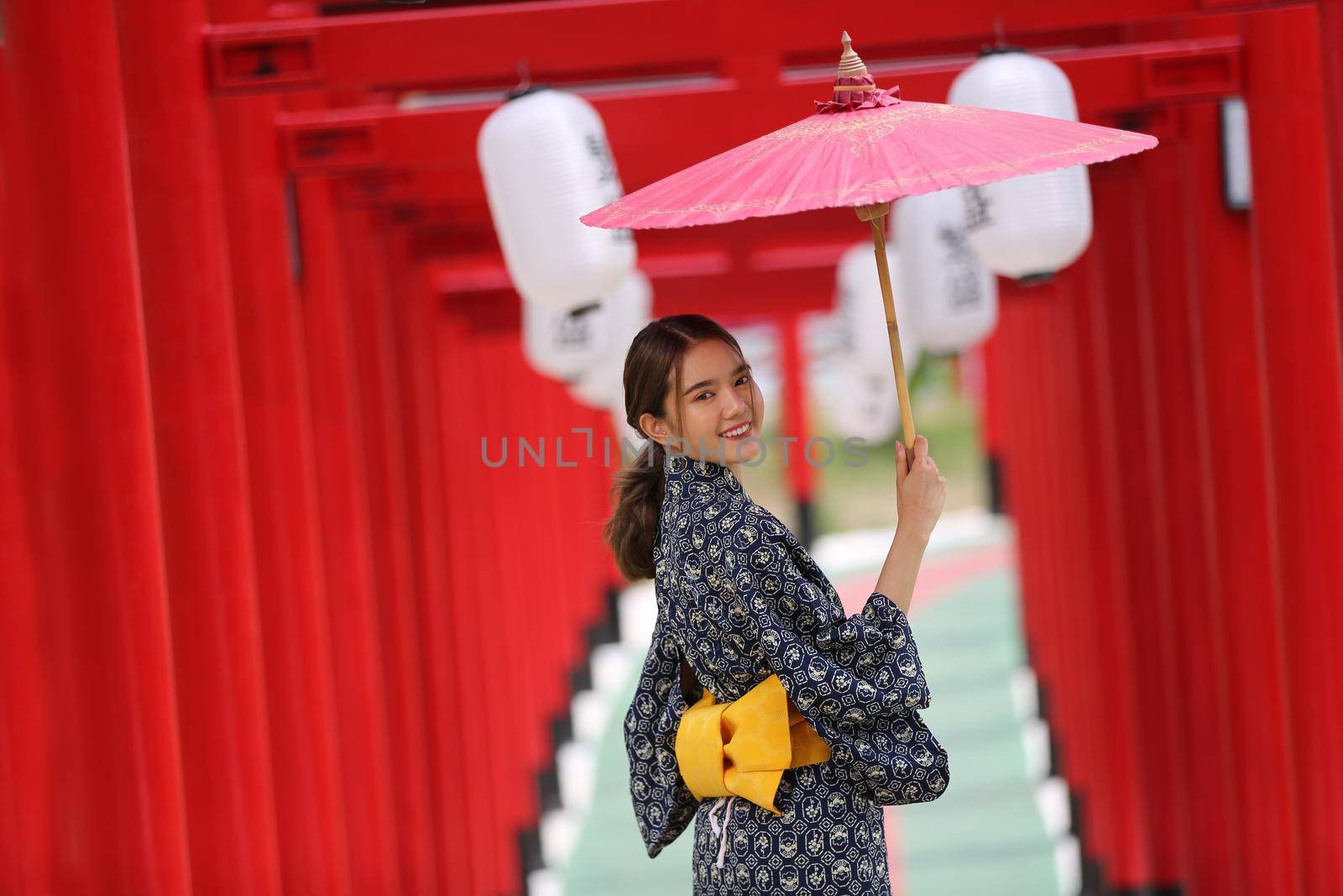 woman in kimono holding umbrella walking into at the shrine red gate, in Japanese garden.