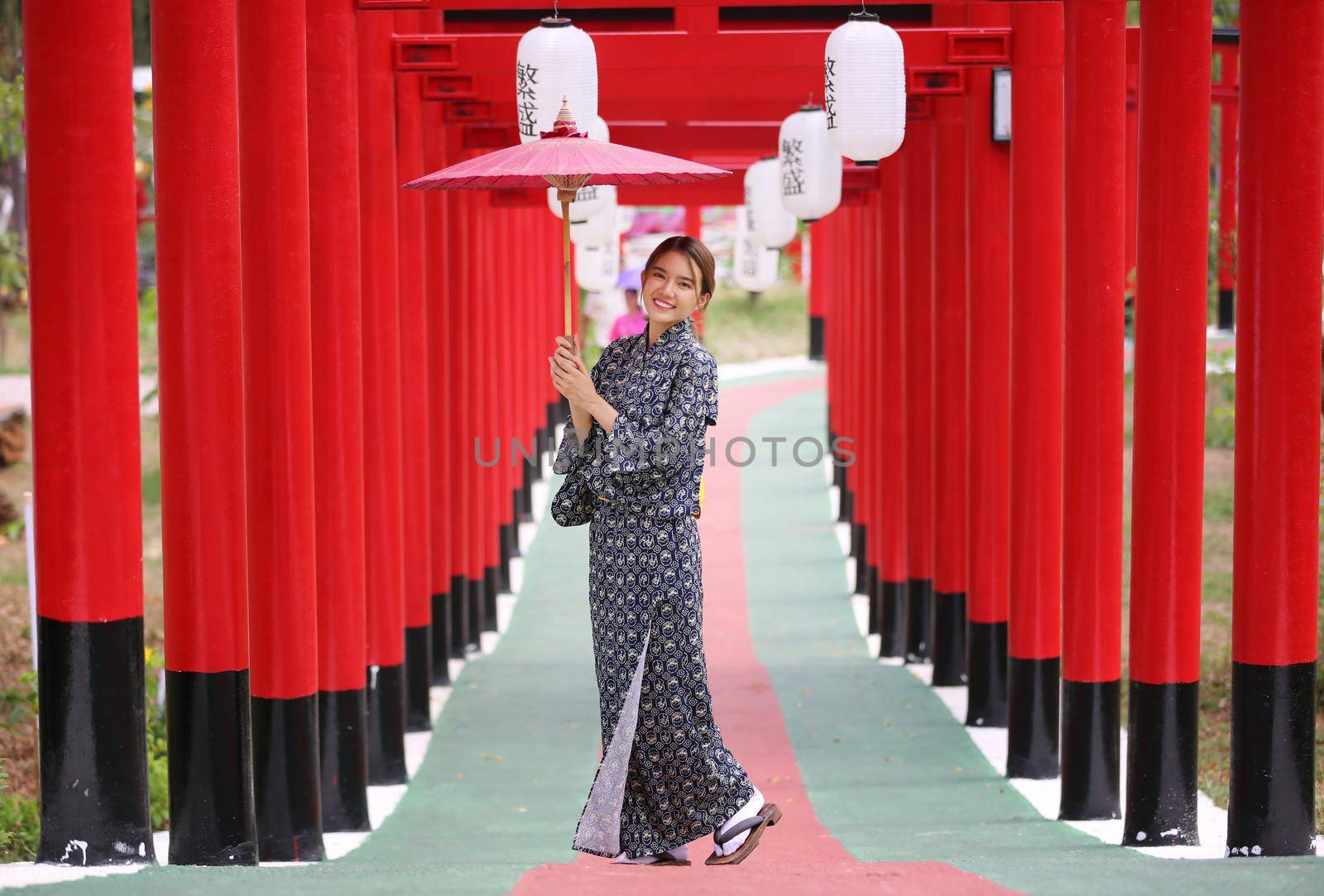 woman in kimono holding umbrella walking into at the shrine red gate, in Japanese garden.
