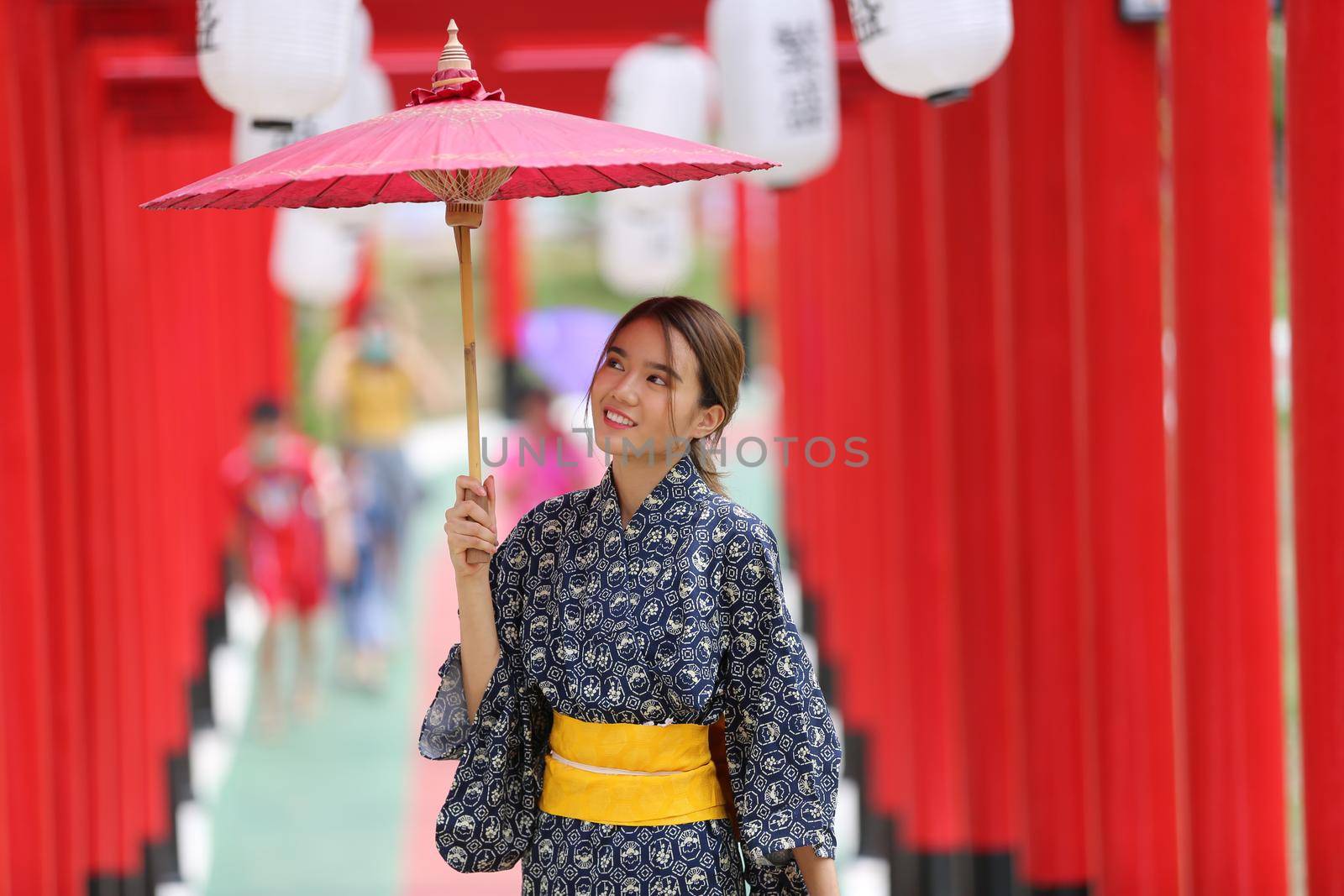 woman in kimono holding umbrella walking into at the shrine red gate, in Japanese garden.