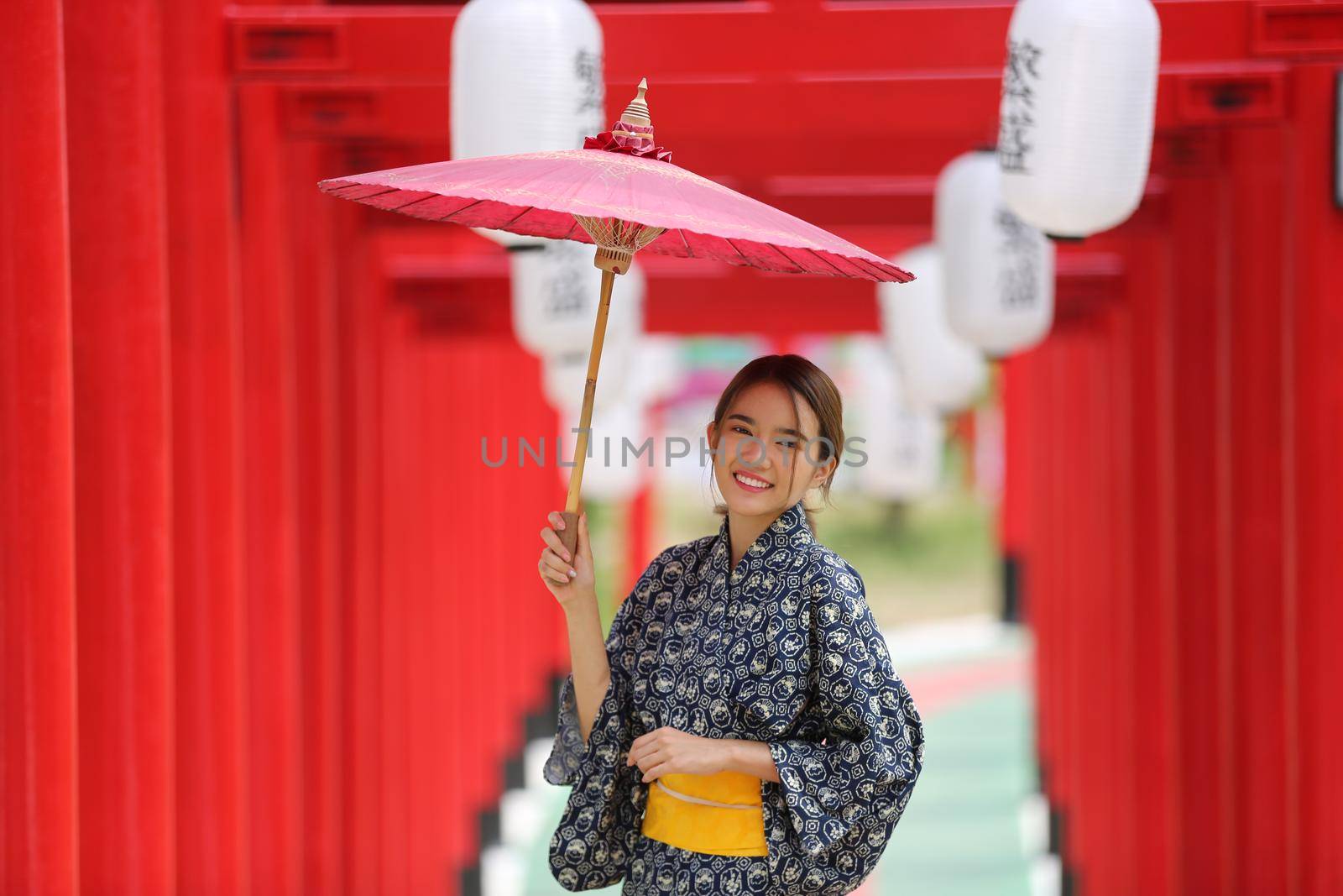 woman in kimono holding umbrella walking into at the shrine red gate, in Japanese garden.