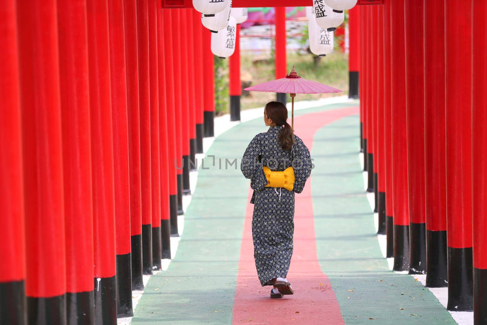 woman in kimono holding umbrella walking into at the shrine red gate, in Japanese garden.