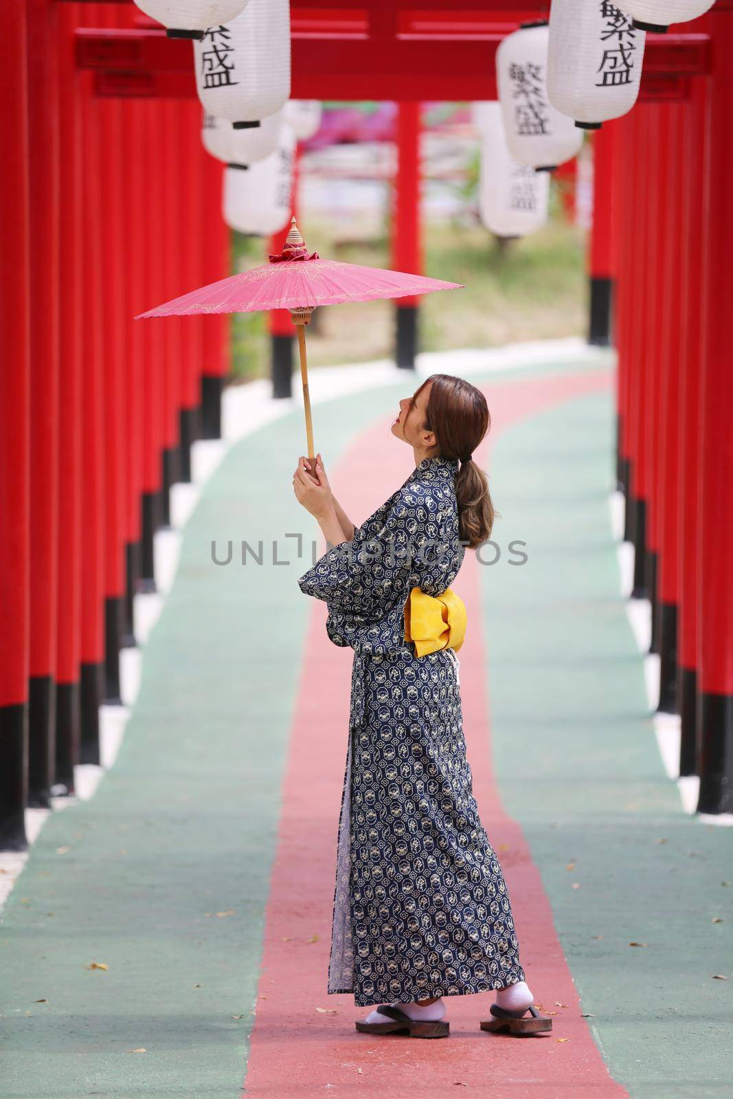 woman in kimono holding umbrella walking into at the shrine red gate, in Japanese garden. by chuanchai