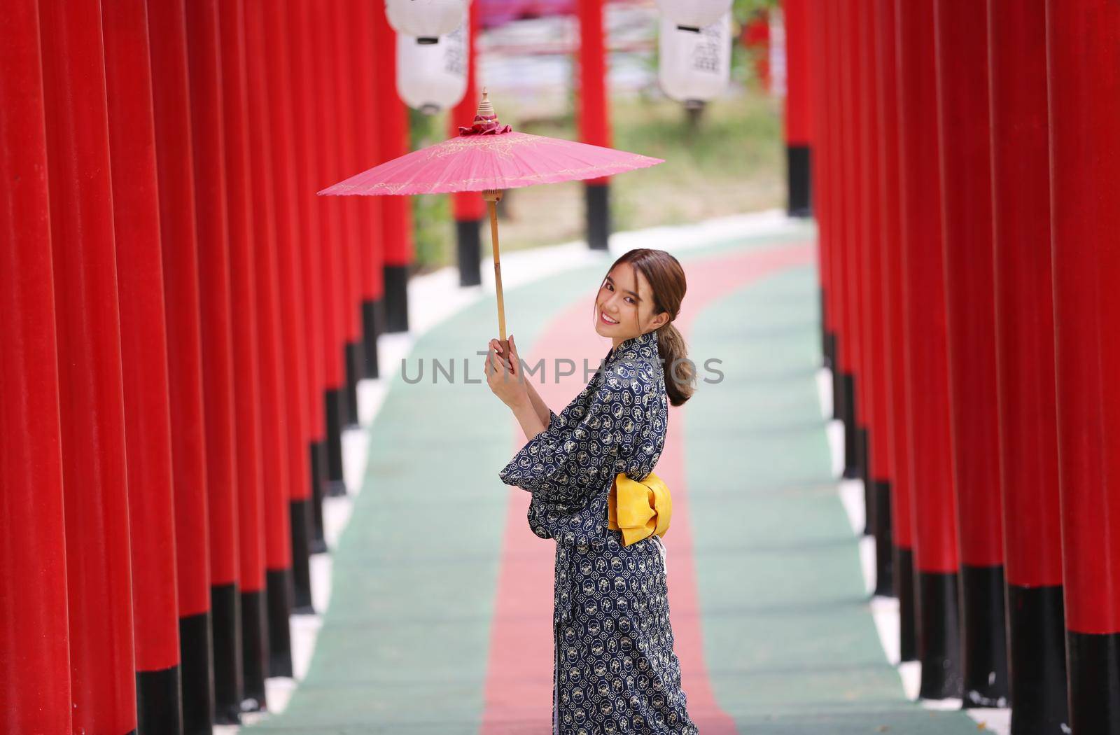 woman in kimono holding umbrella walking into at the shrine red gate, in Japanese garden.