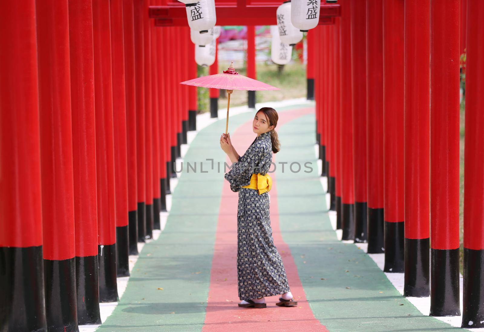 woman in kimono holding umbrella walking into at the shrine red gate, in Japanese garden.